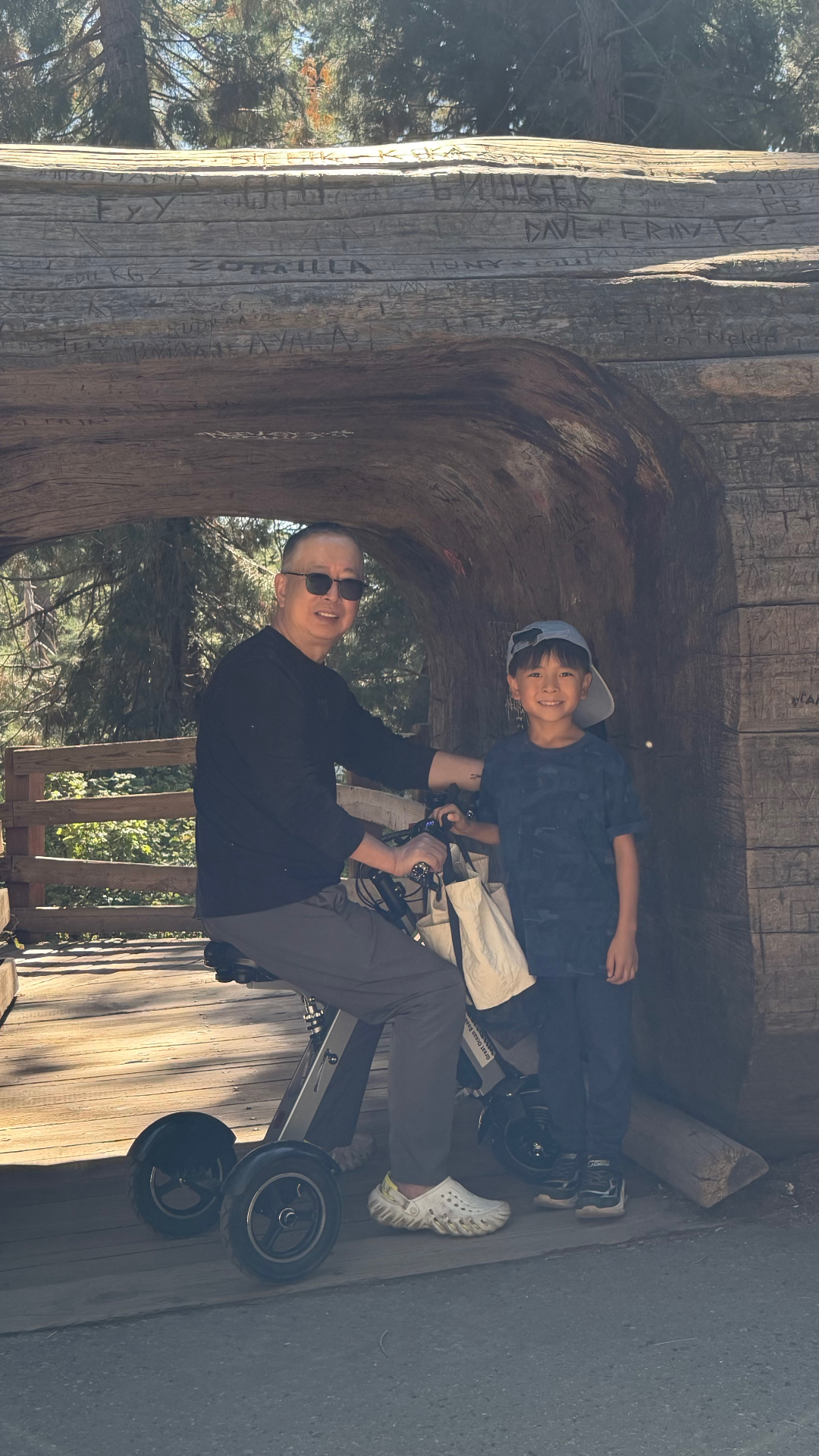 A man on a tricycle and a boy posing inside a hollowed fallen sequoia log