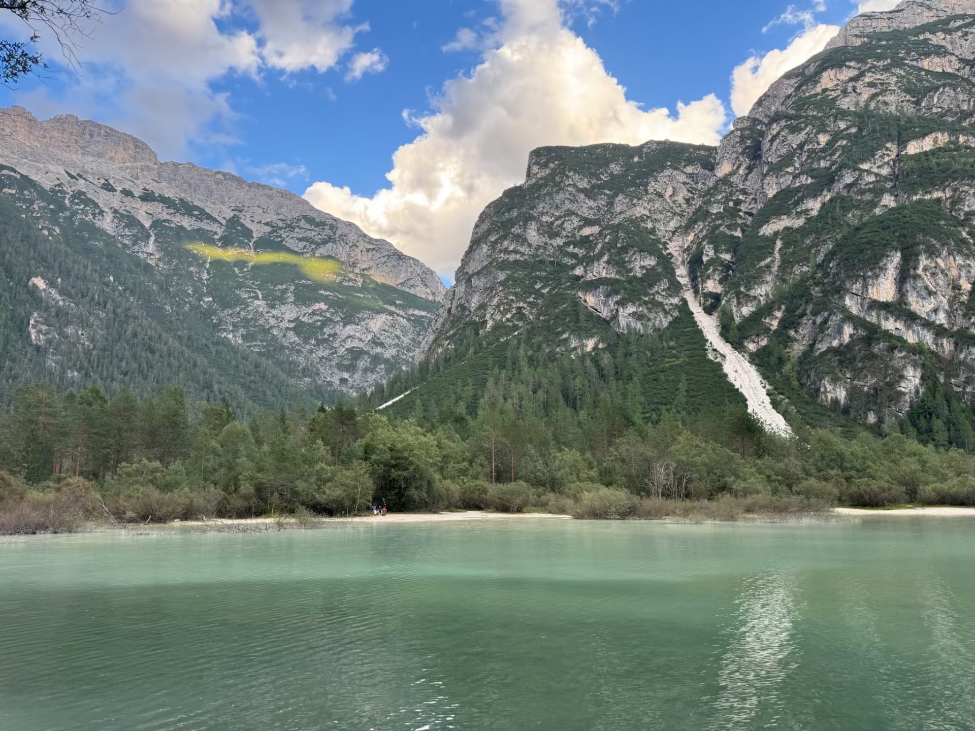 Still turquoise lake bordered by forest and steep green mountain walls