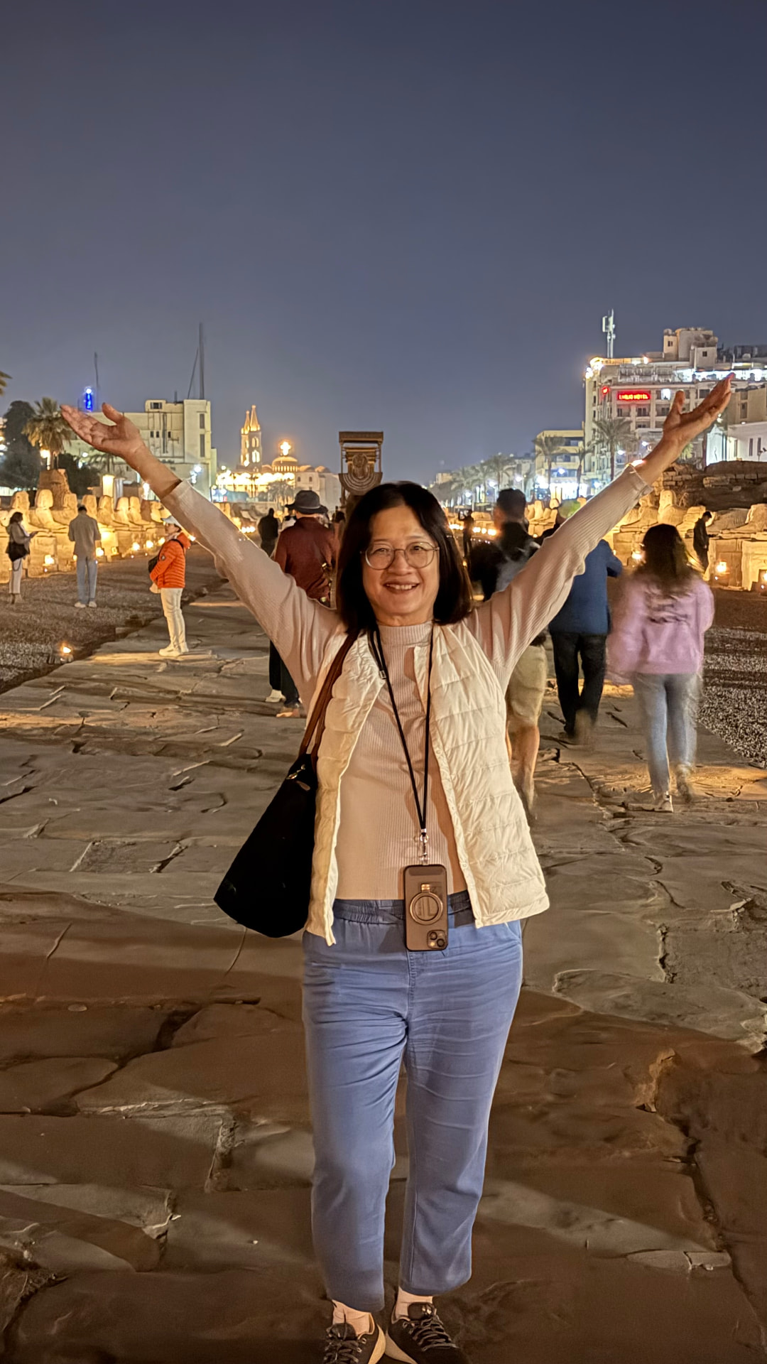 Becky with arms raised standing on the Avenue of the Sphinxes at night