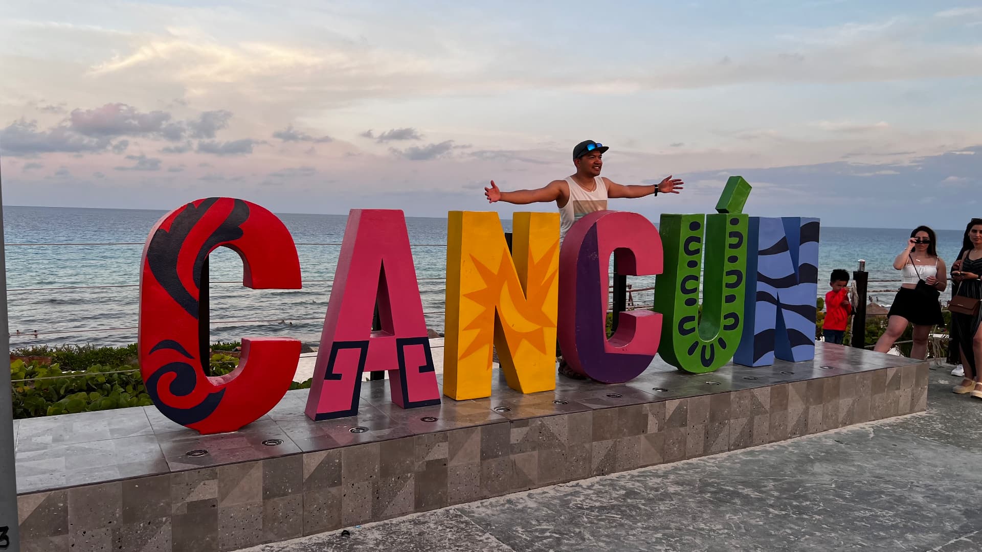 Ken standing behind the colorful Cancún letters beside the sea