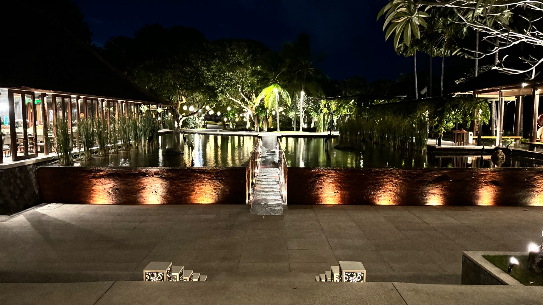 Resort reflecting pond and lit stone causeway at night, with palms behind