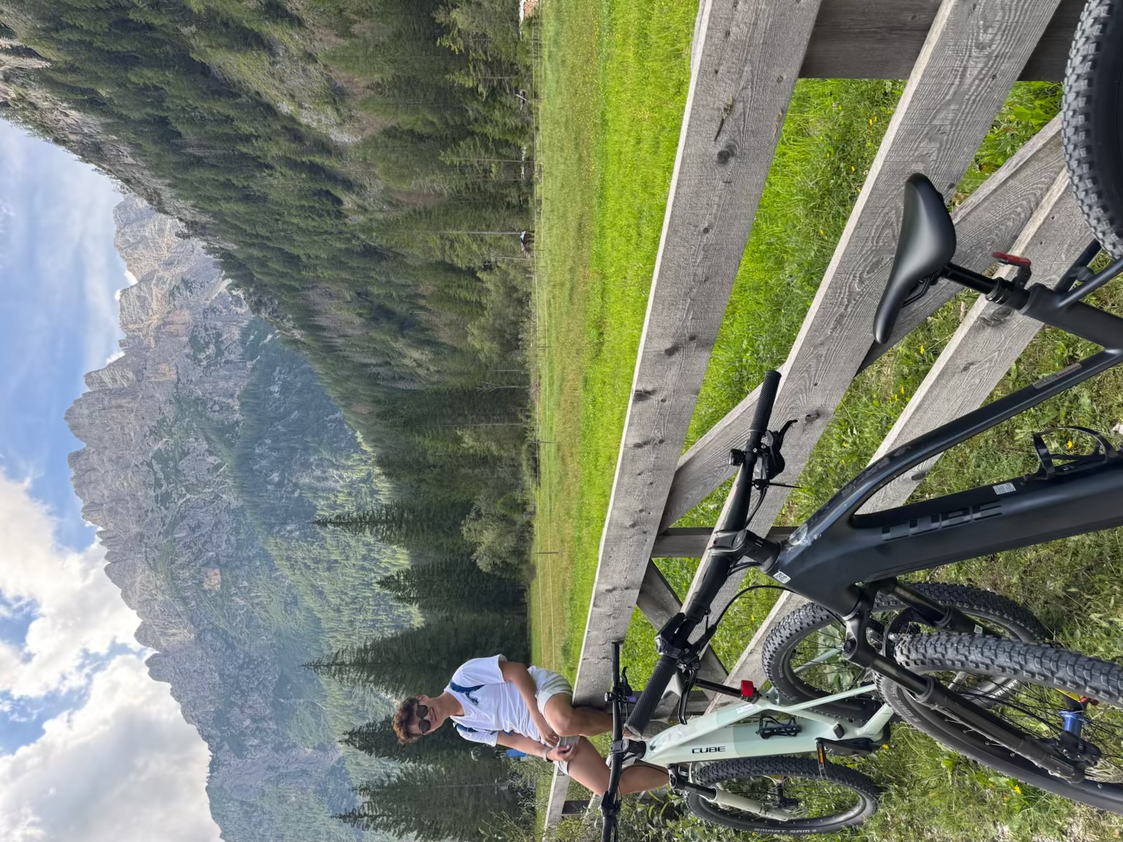 Kayden resting beside two mountain bikes in a green Dolomites meadow
