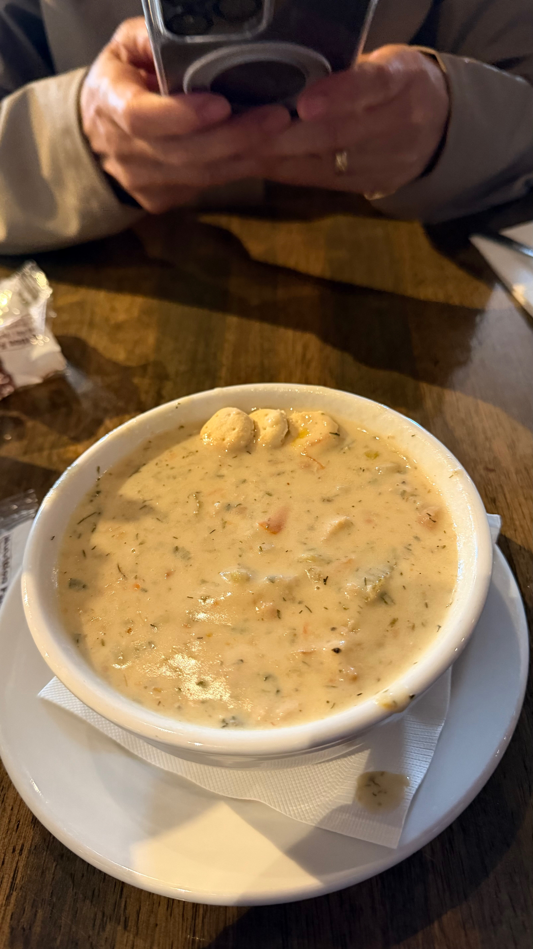 A white bowl of creamy Alaskan seafood chowder with oyster crackers on a wooden table