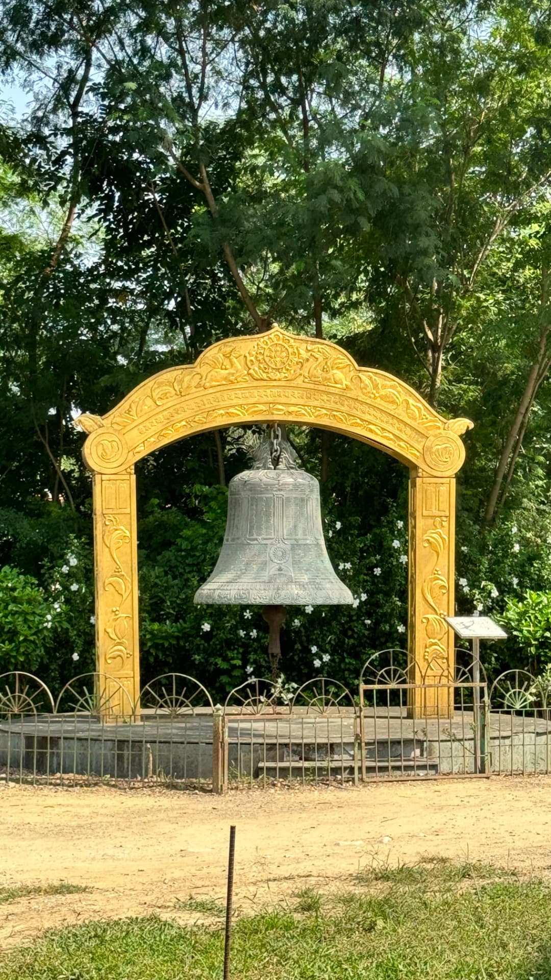 A ceremonial bell hangs beneath an ornate golden arch. — Lumbini, Nepal.