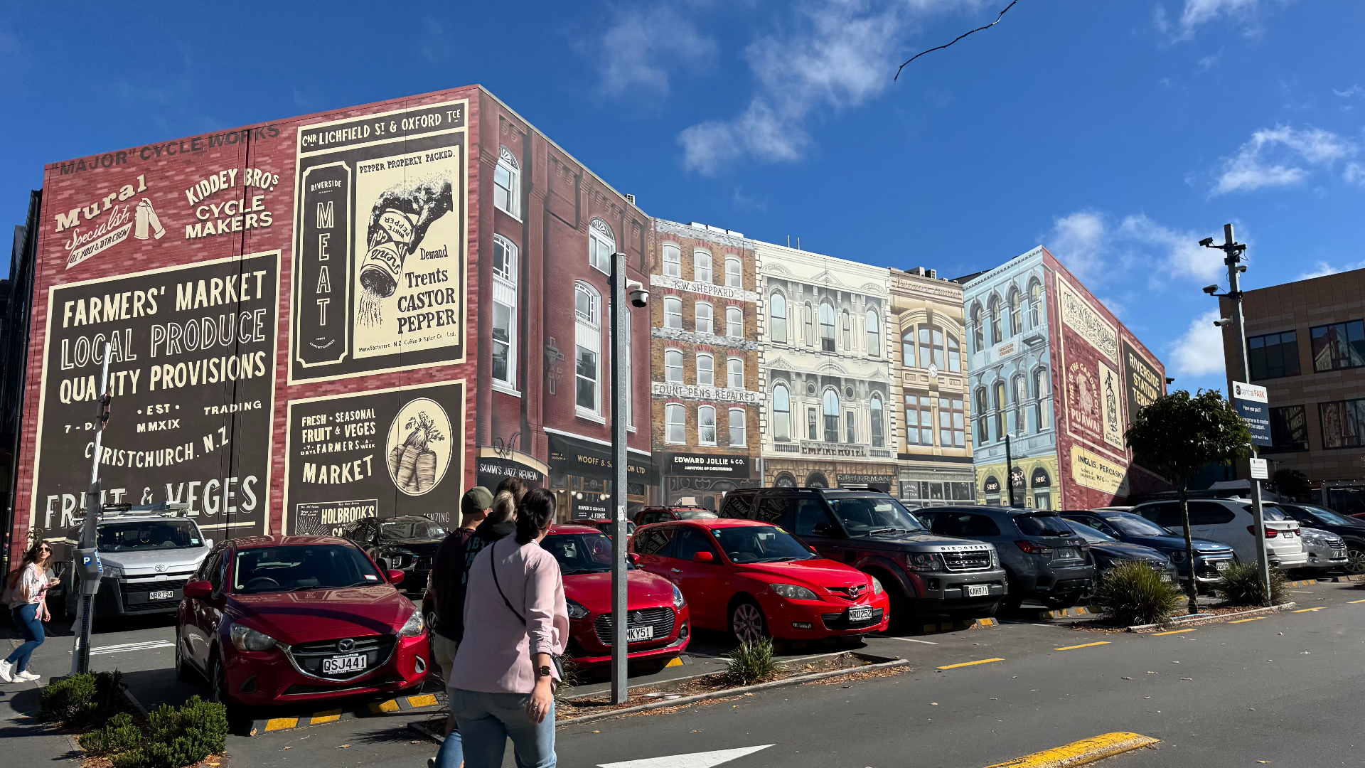 A large heritage-style painted mural of old shopfronts and advertisements on a wall beside a downtown Christchurch car park