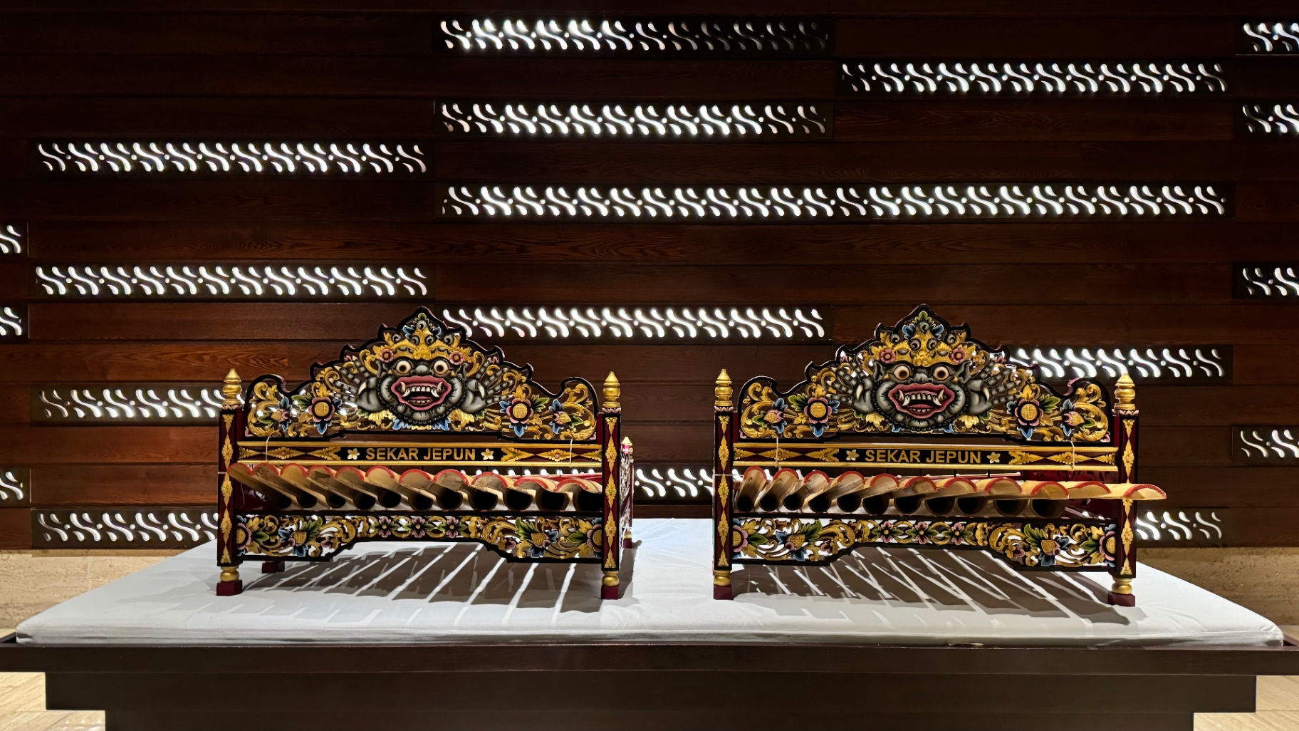 Two ornate Balinese gamelan instruments displayed against a patterned timber wall