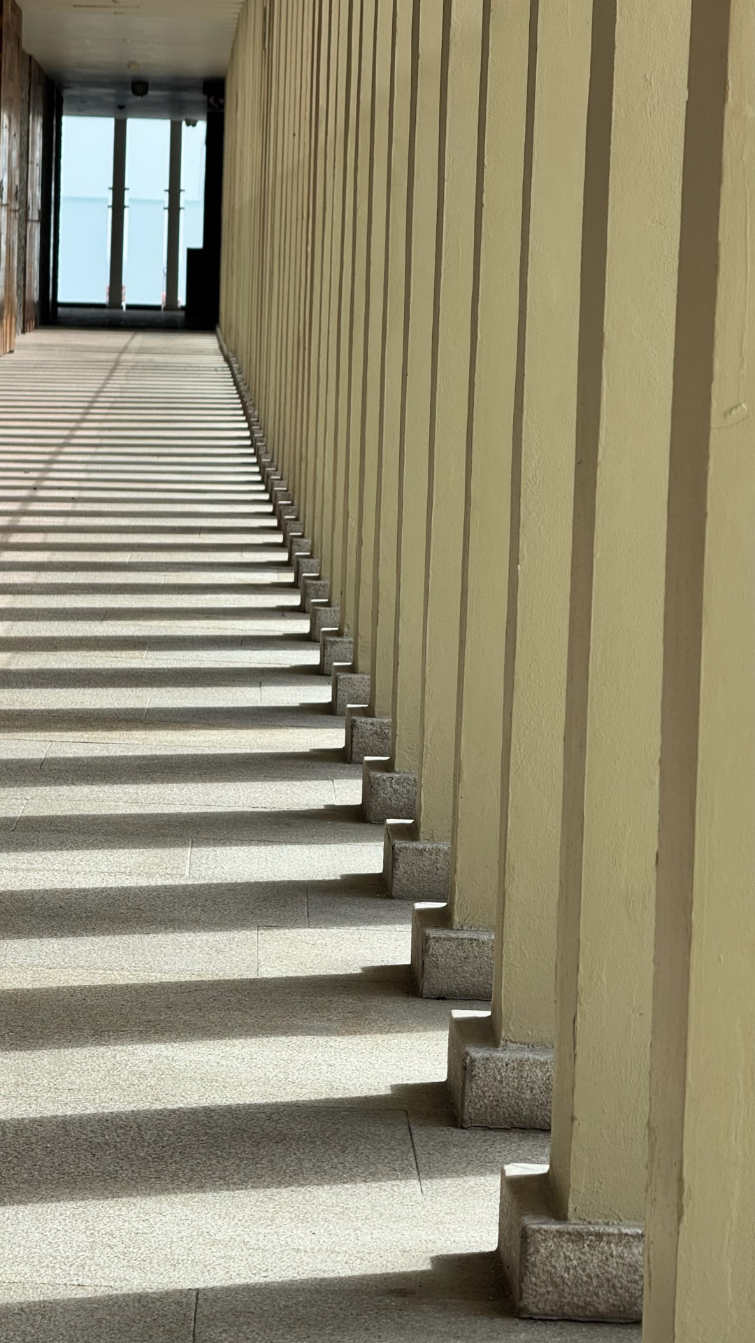 Striped sunlight crossing a long hotel passage toward the sea