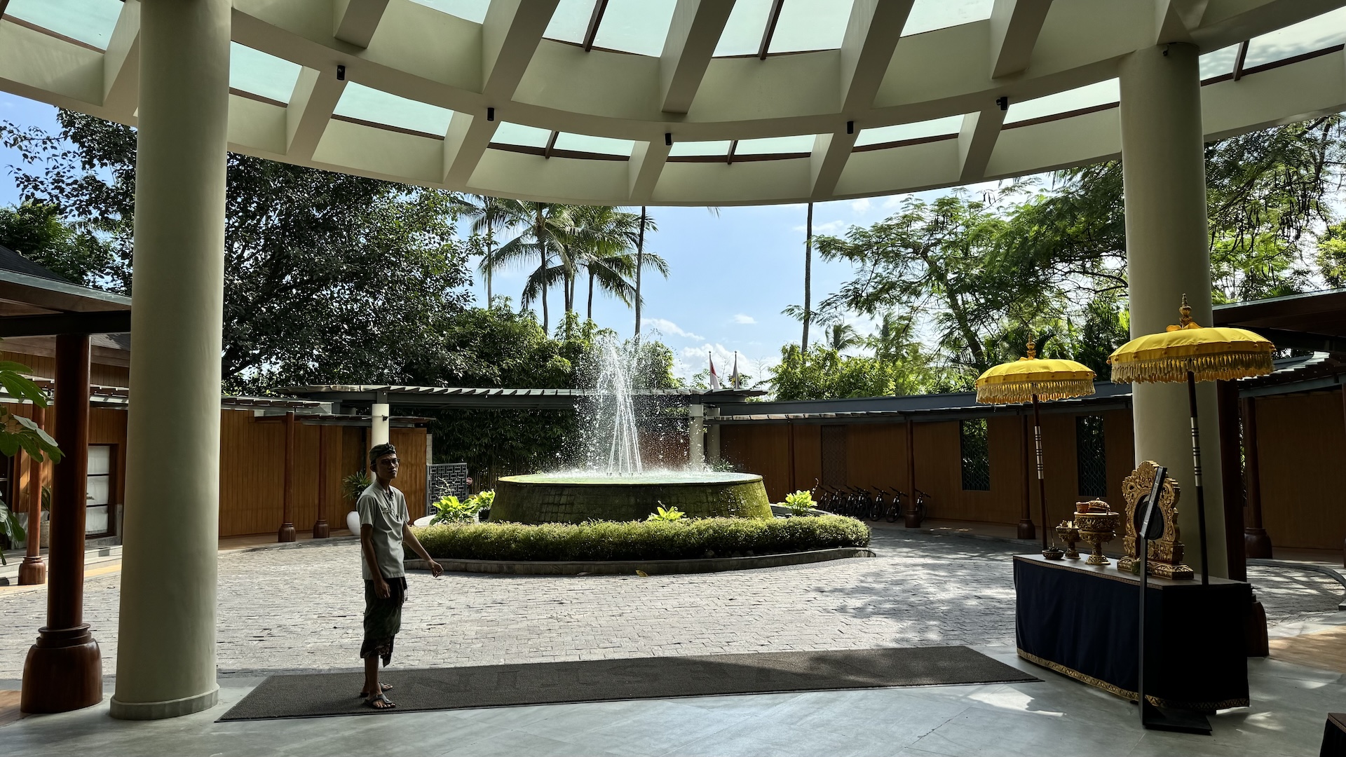 The Westin Ubud arrival pavilion with a circular fountain, palms and yellow Balinese parasols