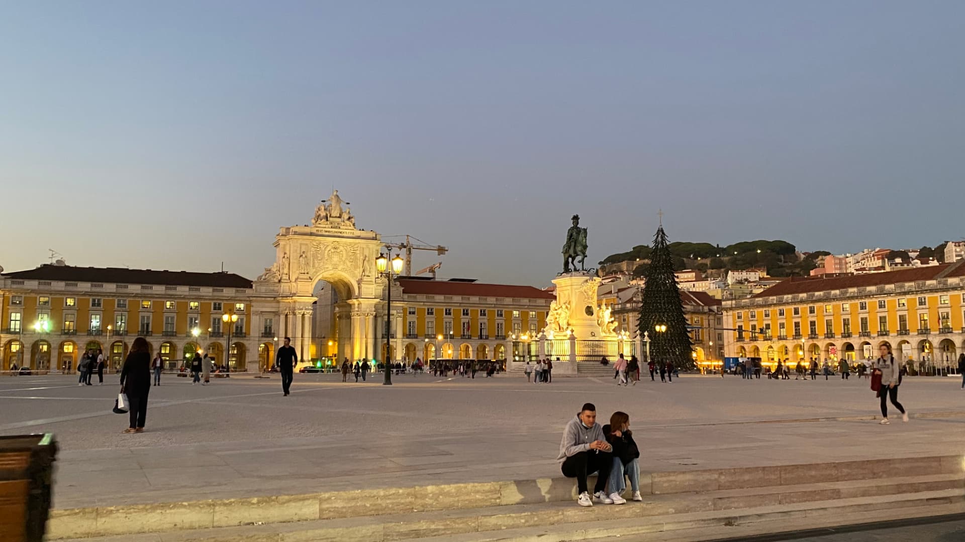 Praça do Comércio at dusk with people walking between the buildings
