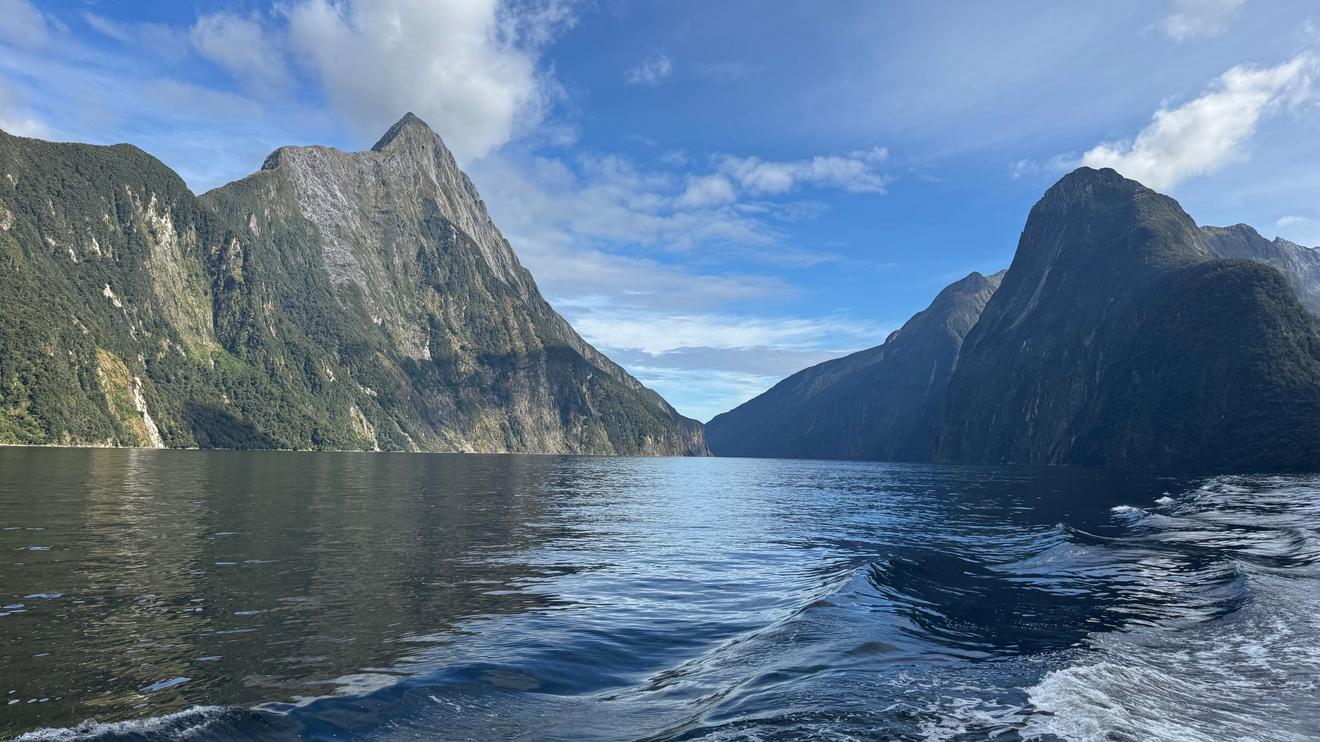 A view of Mitre Peak rising from still dark water, captured from the back of a cruising boat with its white wake in the foreground