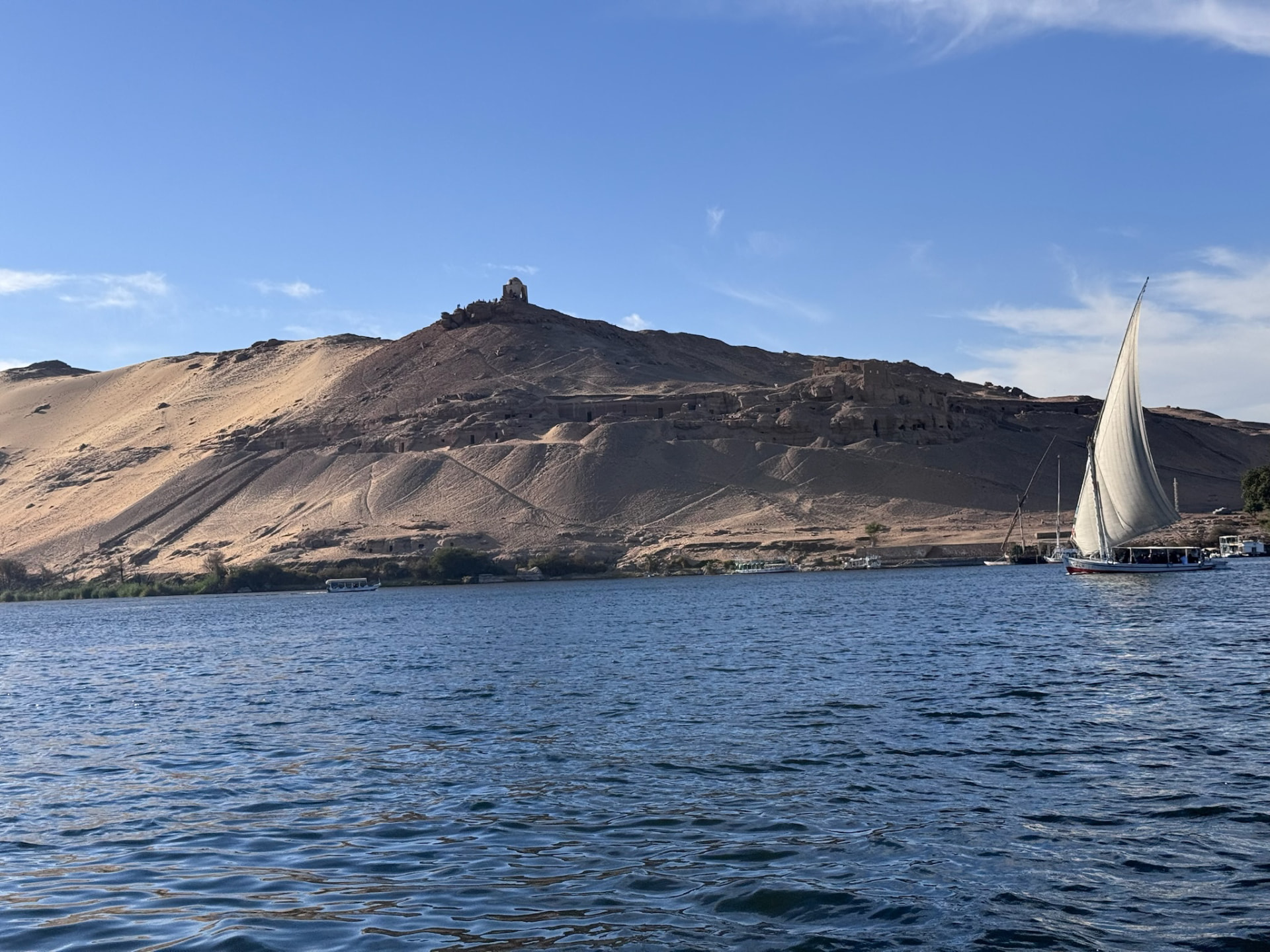 A felucca under full sail on the Nile with the sand hills and tombs of the west bank behind