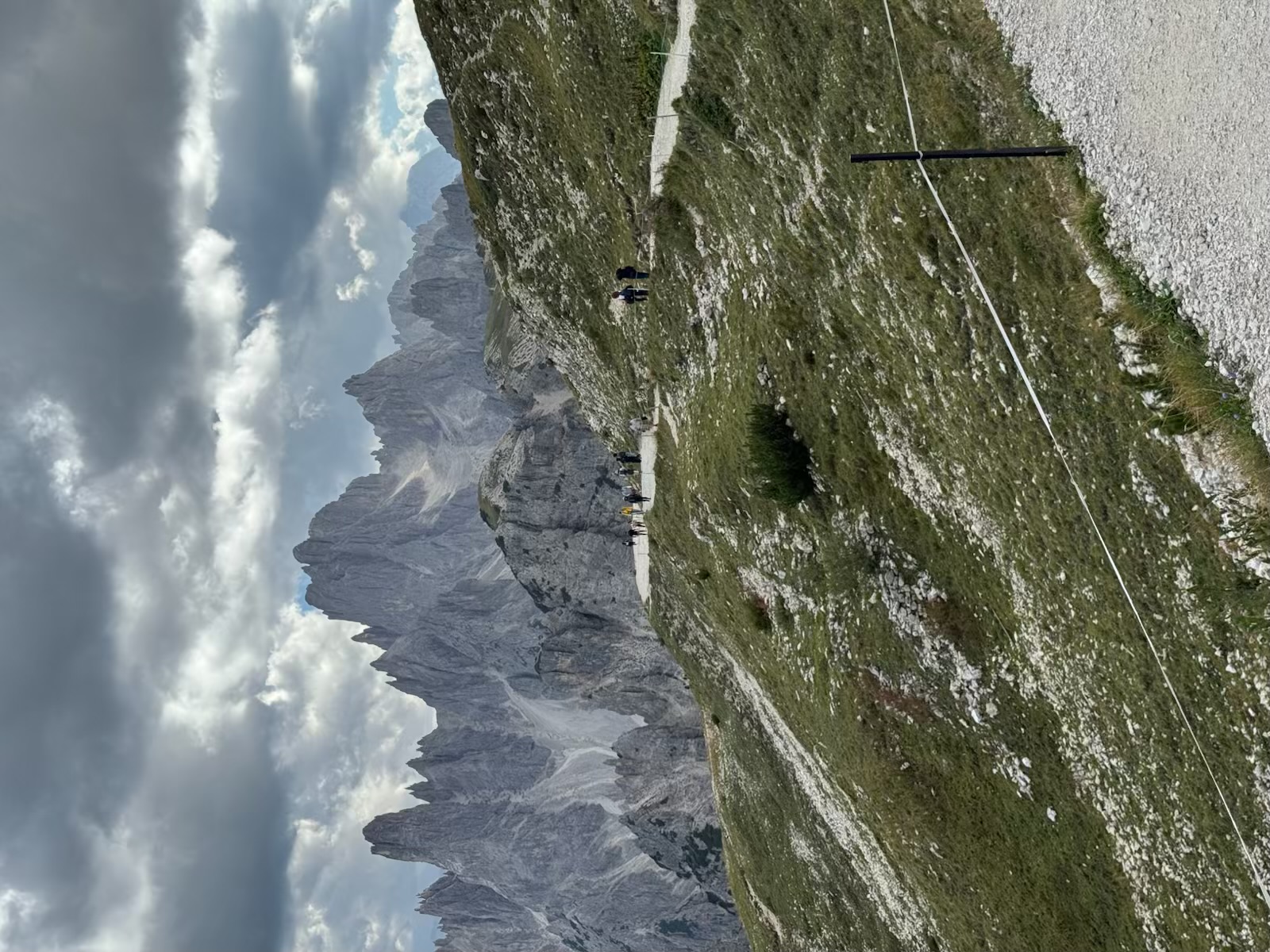 Hikers following a ridge path toward sharp grey Dolomites peaks beneath storm clouds