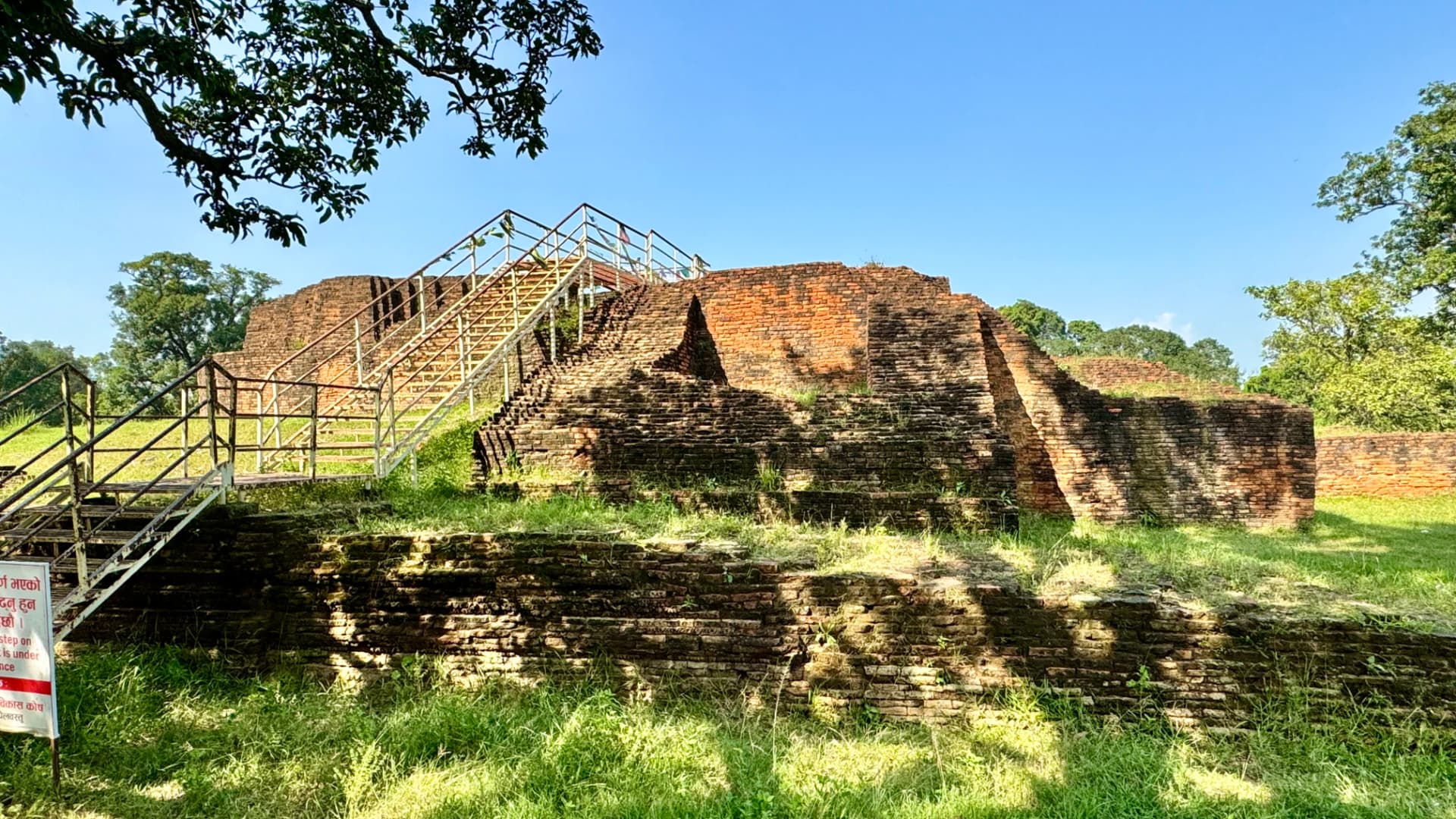 Ancient brick remains rise above a green lawn. — Sacred sites near Lumbini, Nepal.