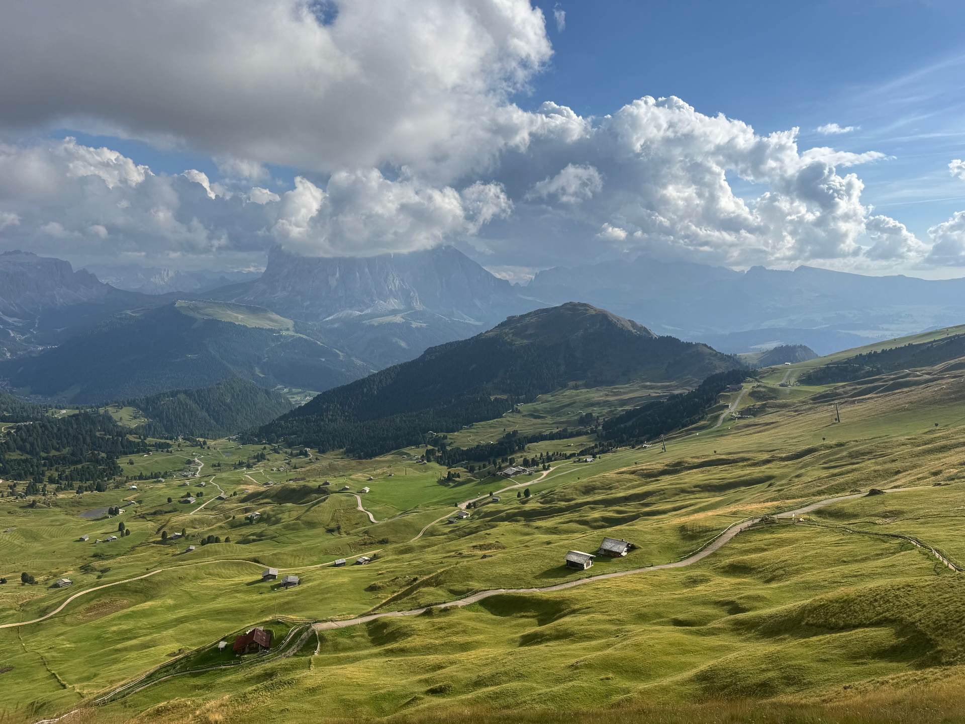 Wide green alpine valley beneath towering clouds and distant Dolomites ridges