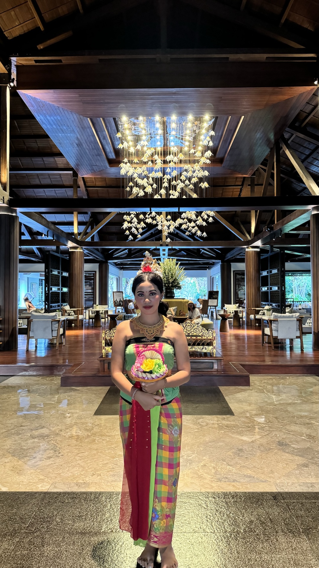 Balinese hostess standing beneath a cascading lobby chandelier