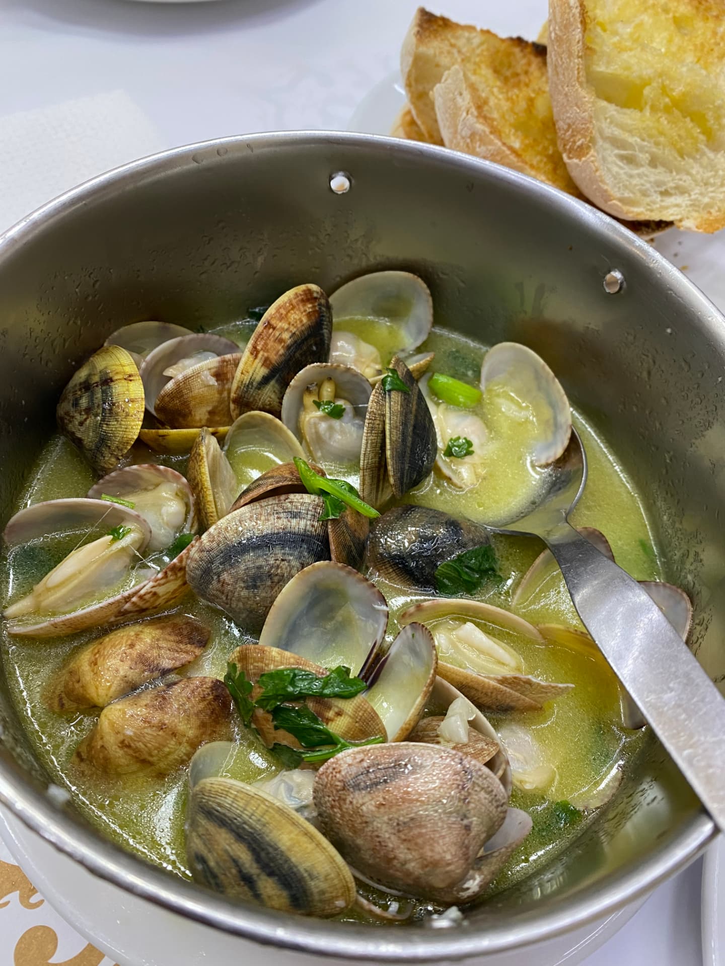Clams cooked in green broth and served in a metal bowl