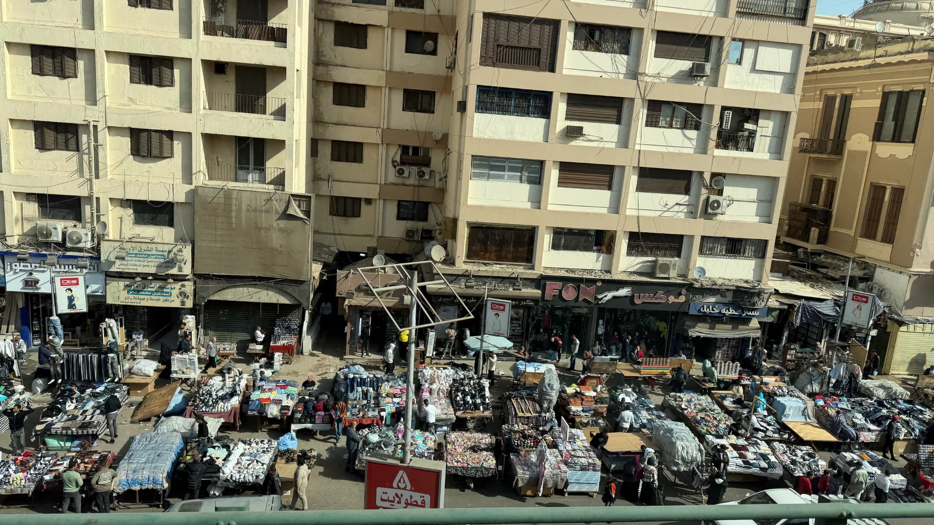 A busy Cairo street market seen from above, with tables of clothing stretching along the road beneath apartment blocks