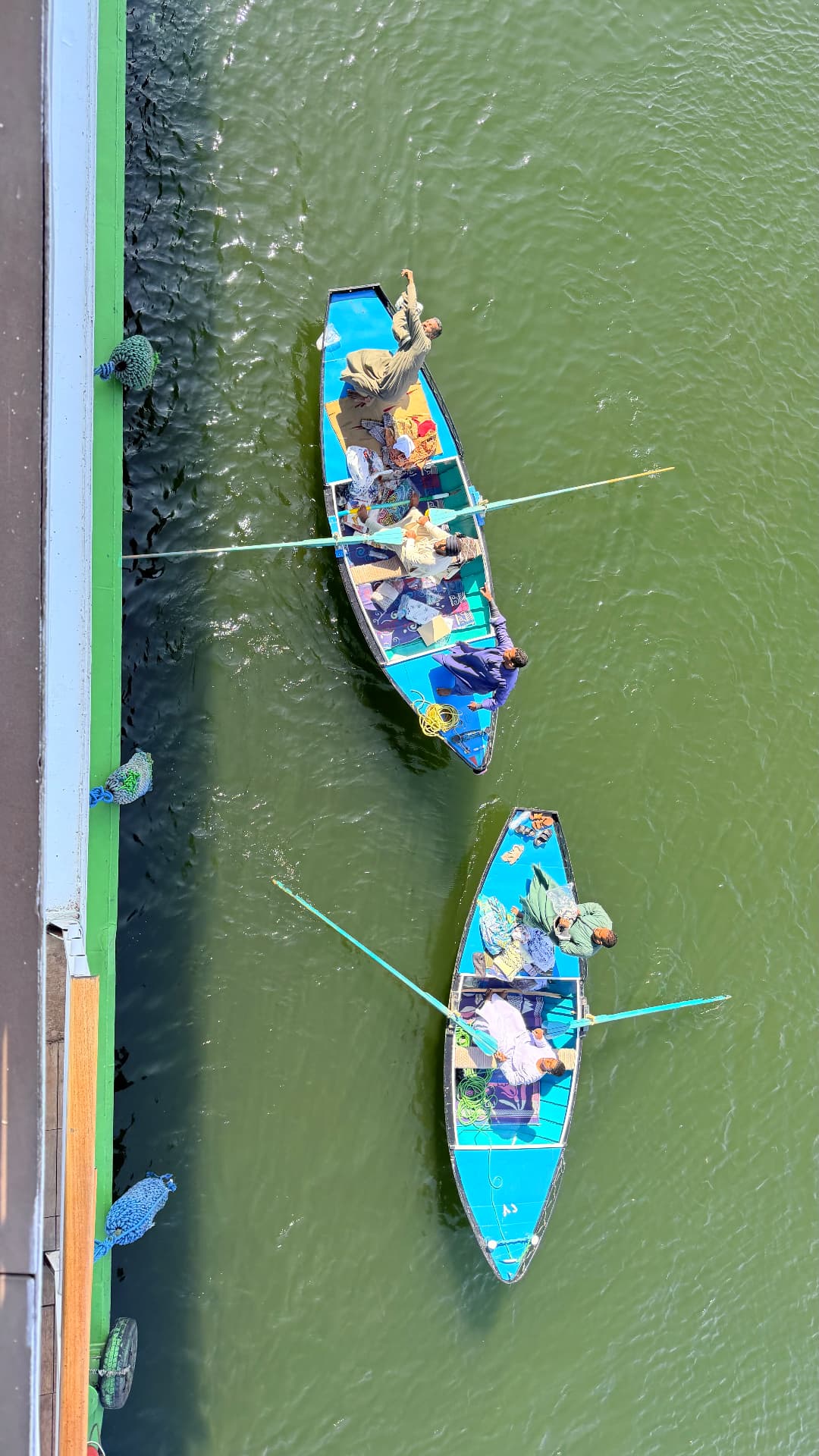 Two blue rowing boats loaded with textiles seen from a ship's deck alongside the green hull