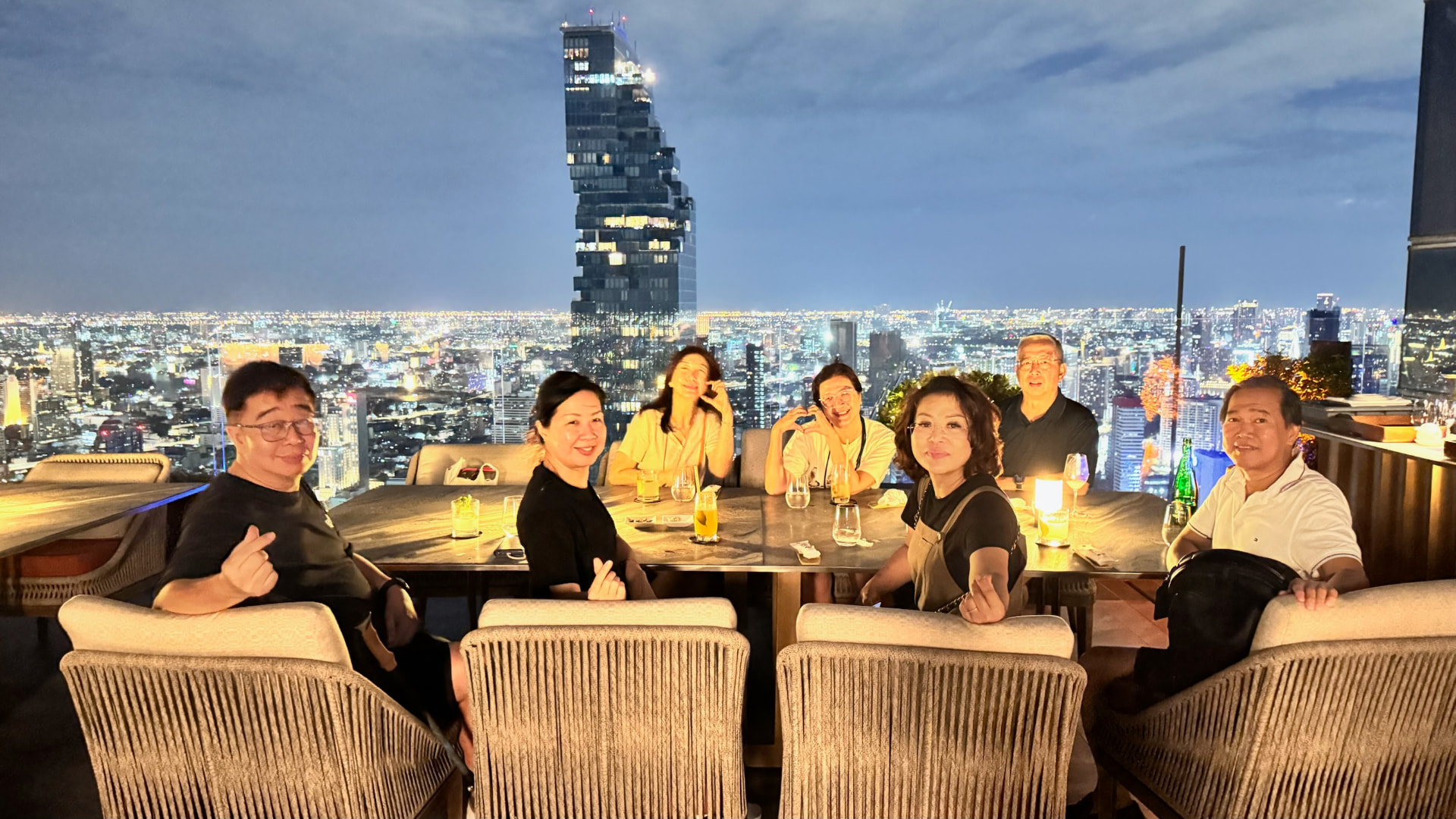 Friends seated at a rooftop table above the Bangkok skyline
