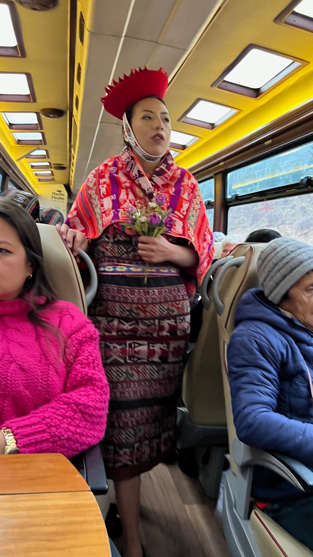 Female performer in traditional Andean clothing holding flowers aboard the Machu Picchu train