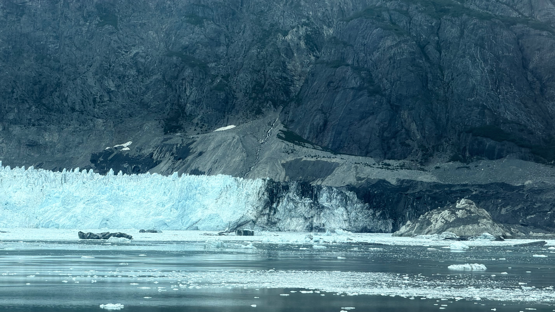 Blue glacier ice, dark moraine and floating fragments beneath a high rock wall