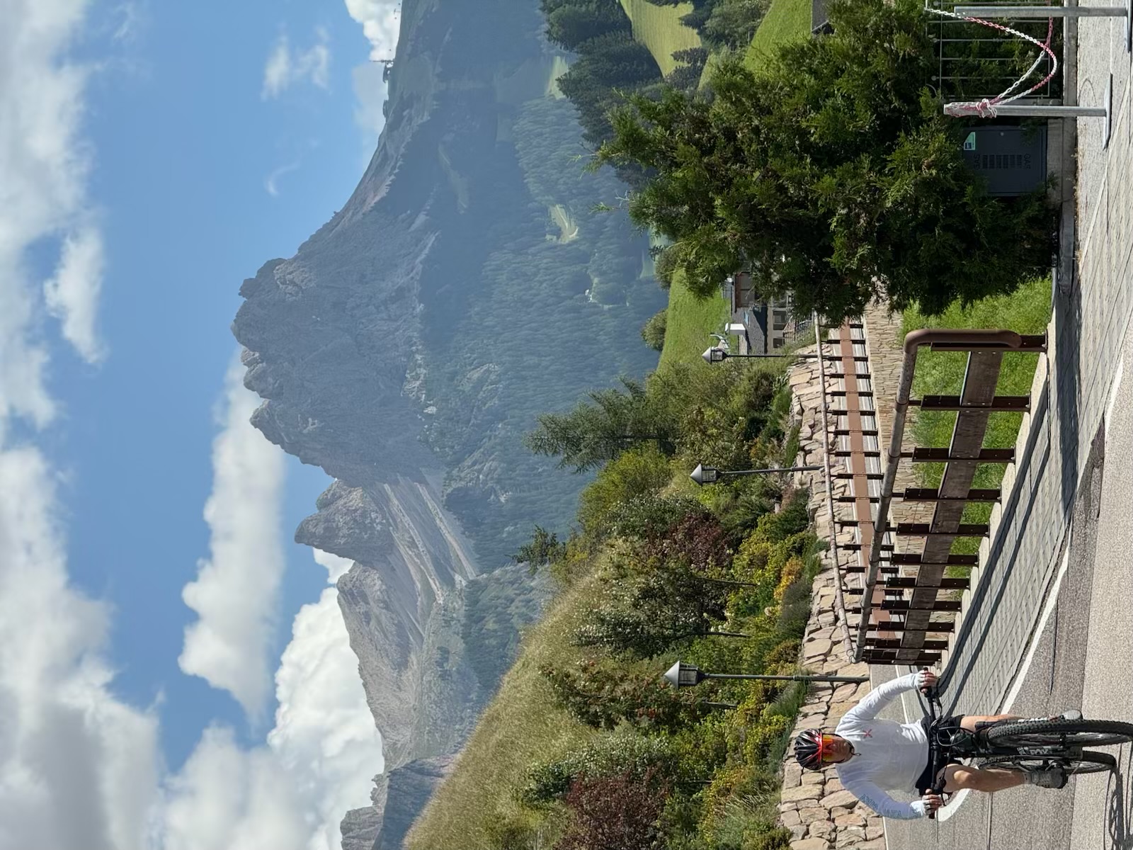 Ken cycling uphill beneath a dramatic Dolomites peak on a clear morning