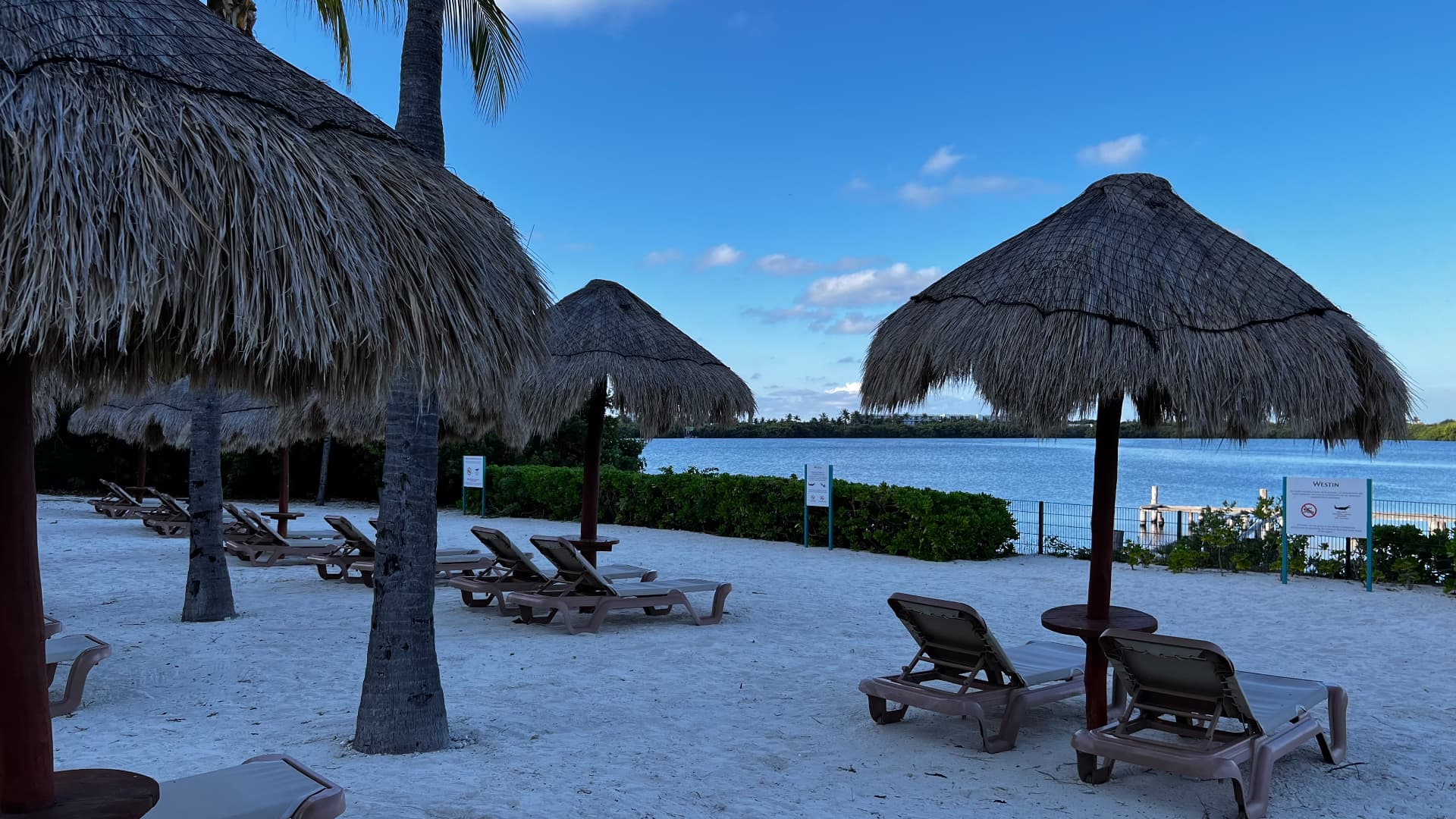 Quiet lagoon beach with empty chairs beneath palapa umbrellas