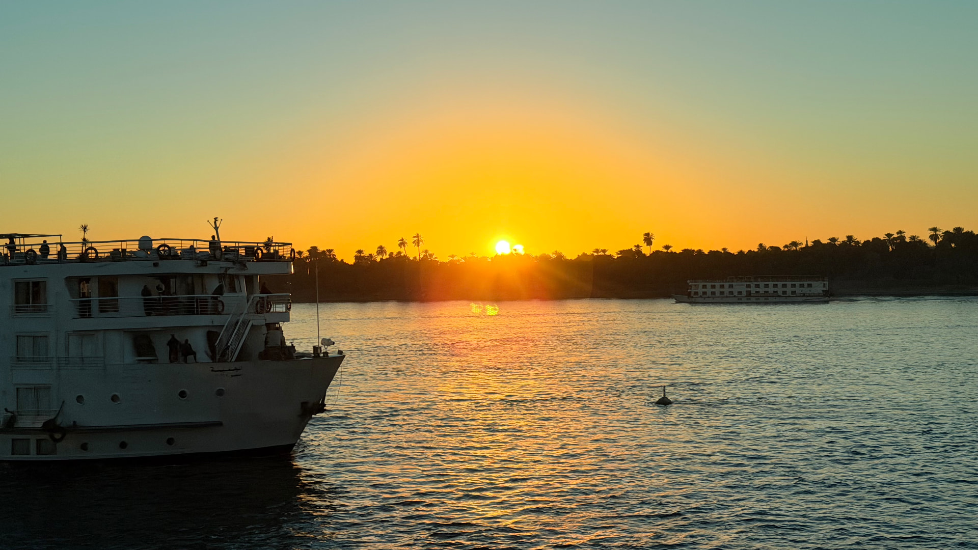 The Nile at sunset with a cruise boat in the foreground and the sun sitting on a line of palms