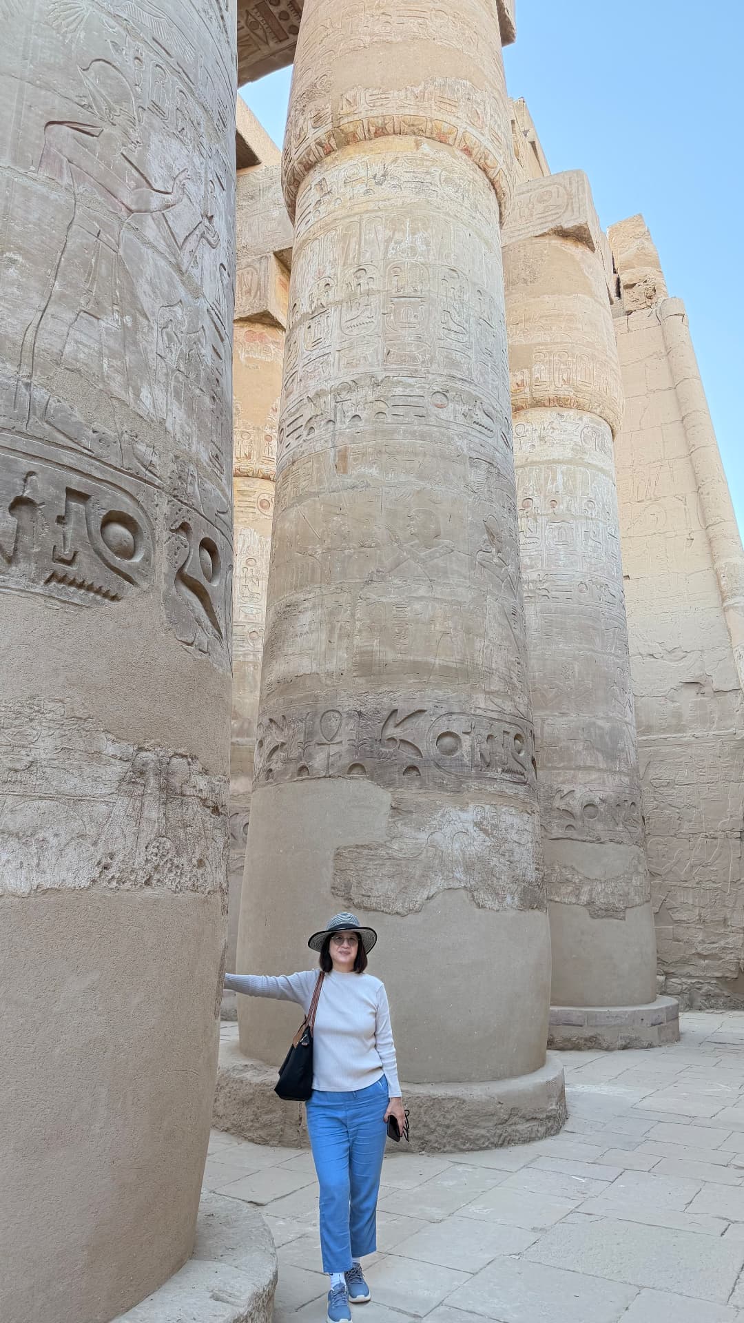 Becky standing at the base of an enormous carved column at Karnak, arm outstretched