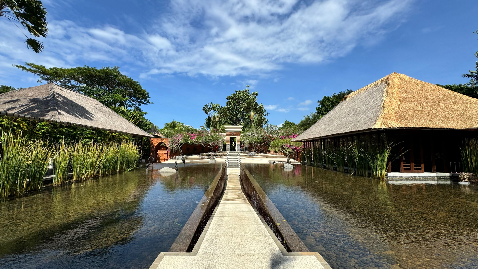Thatched pavilions either side of a wide reflecting pond under a blue sky