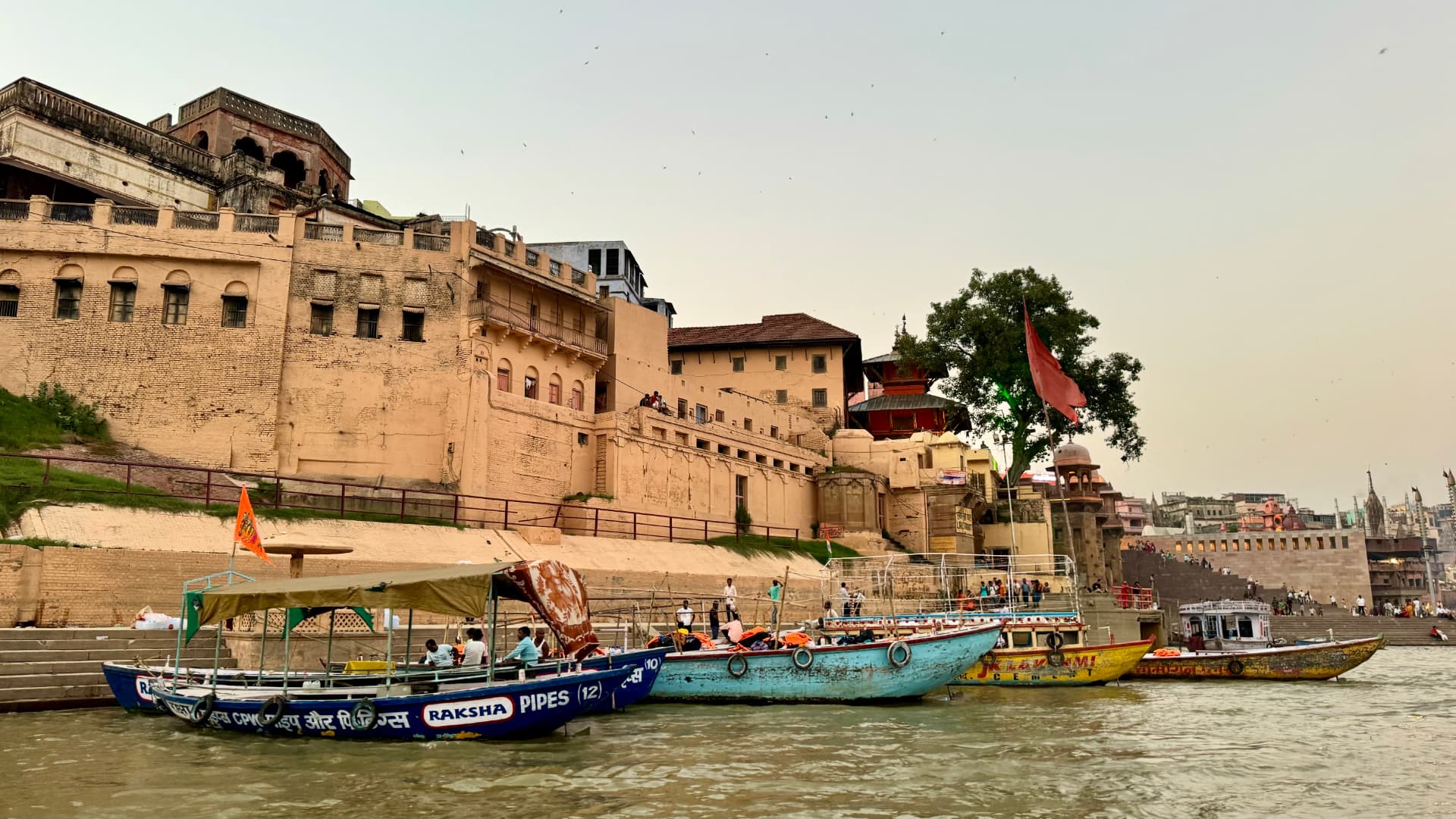 Moored boats lie beneath the sunlit riverfront walls. — Varanasi, Uttar Pradesh, India.