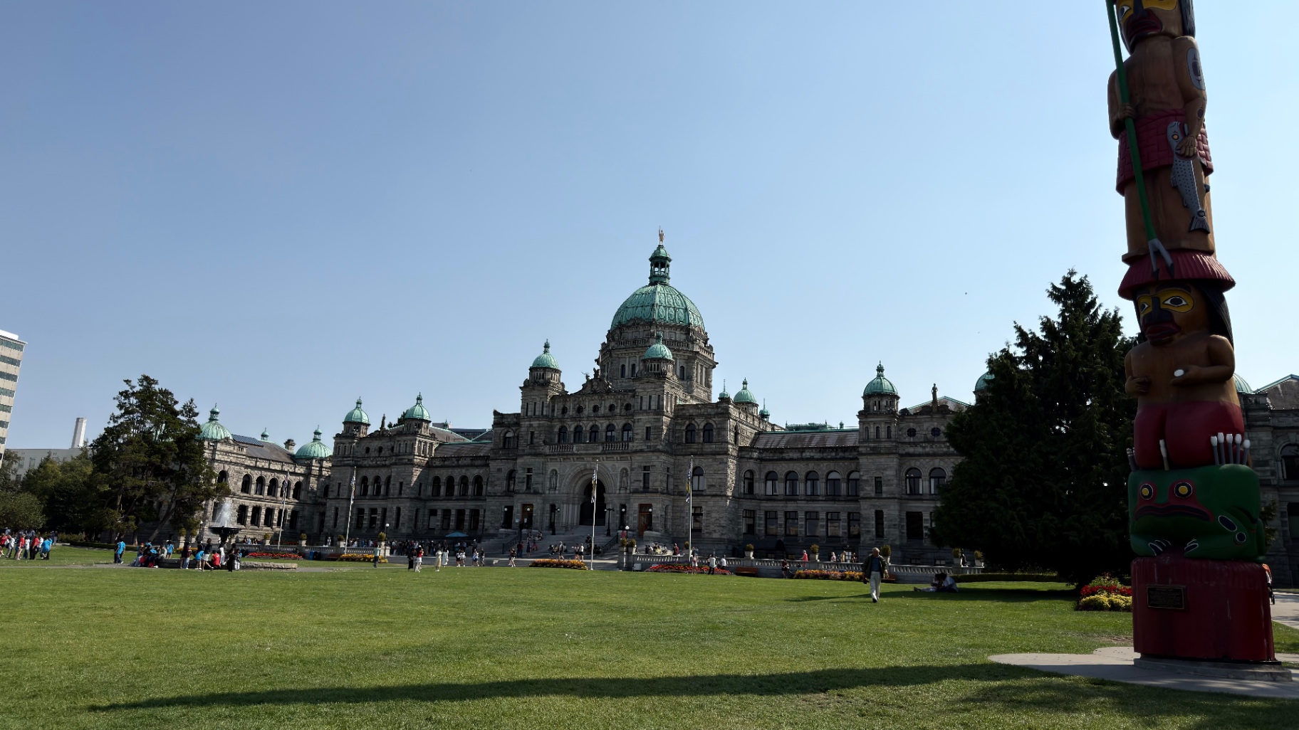 British Columbia Parliament Buildings with green domes and a carved totem pole in the foreground