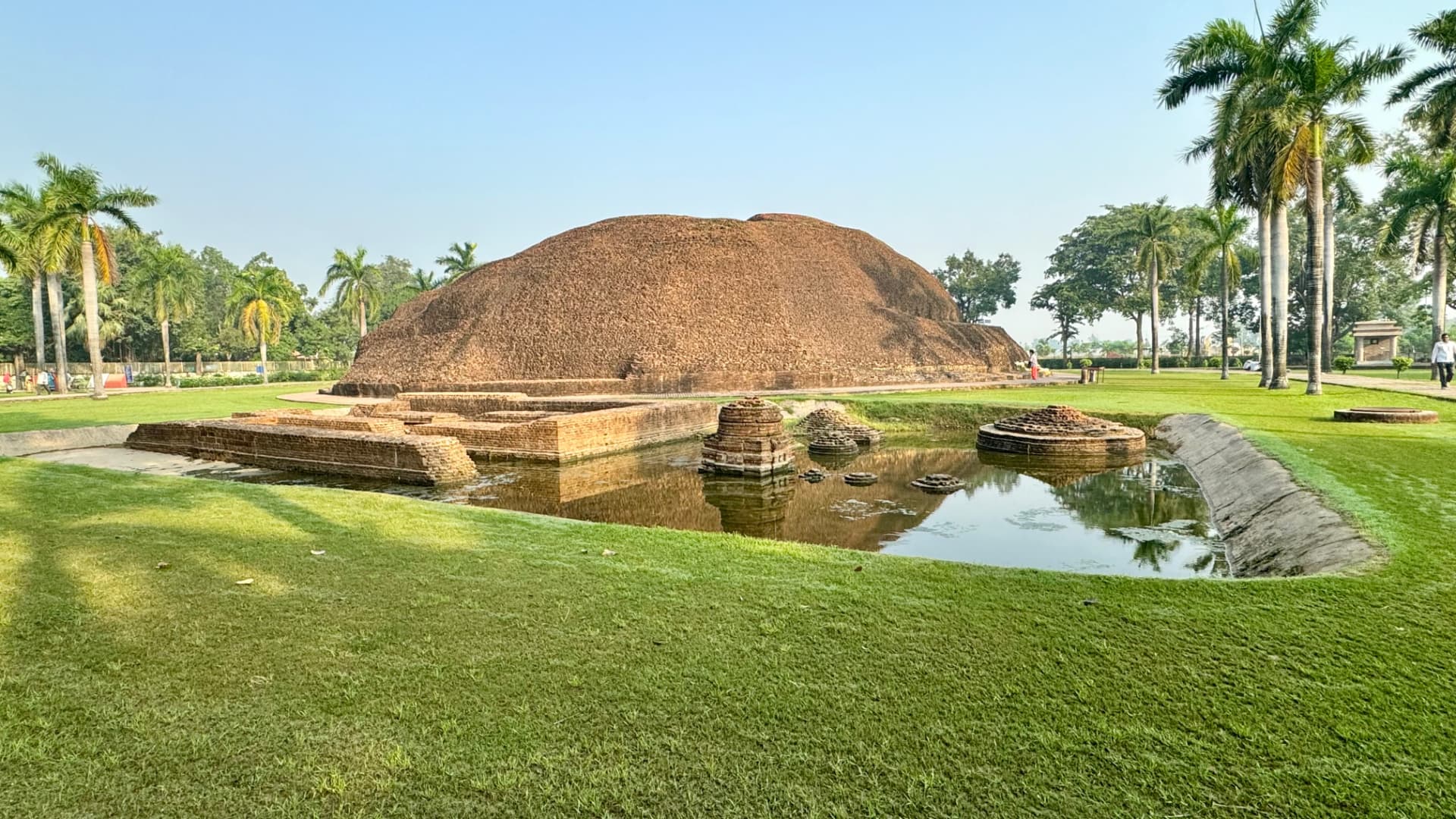 The rounded brick mound of Ramabhar Stupa amid lawns and palms. — Kushinagar, Uttar Pradesh, India.