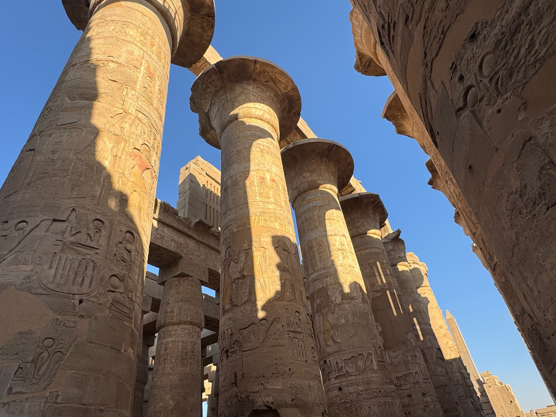 Looking up at the painted columns of the hypostyle hall at Karnak against a blue sky