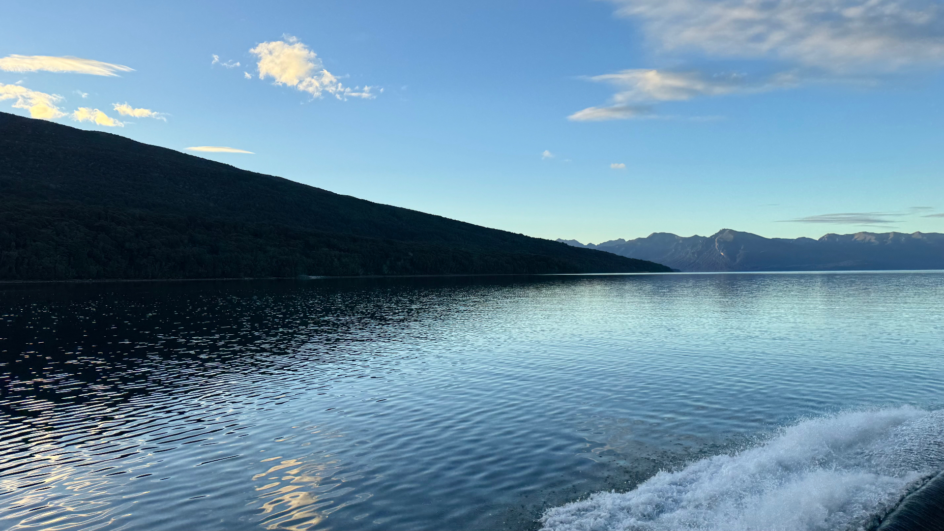 The wake of a boat crossing Lake Te Anau toward distant mountains