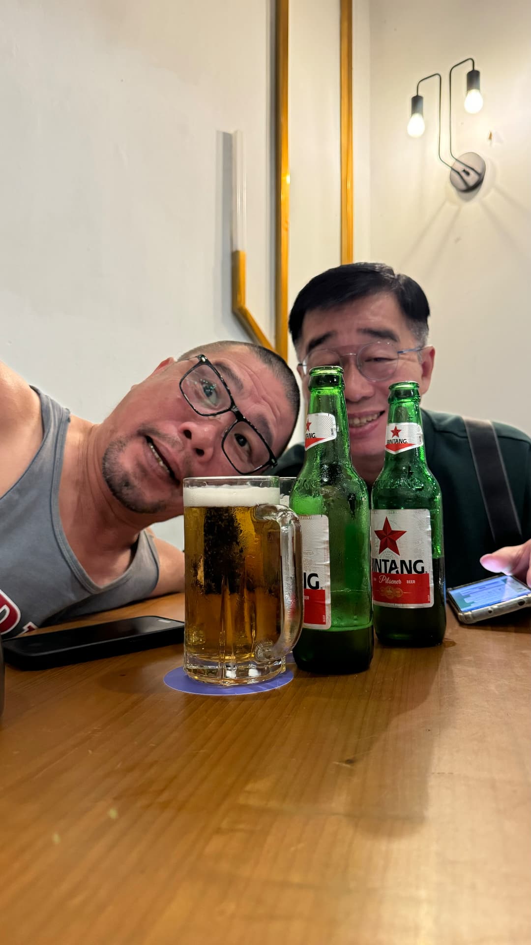 Two companions smiling over bottles of Bintang at a table