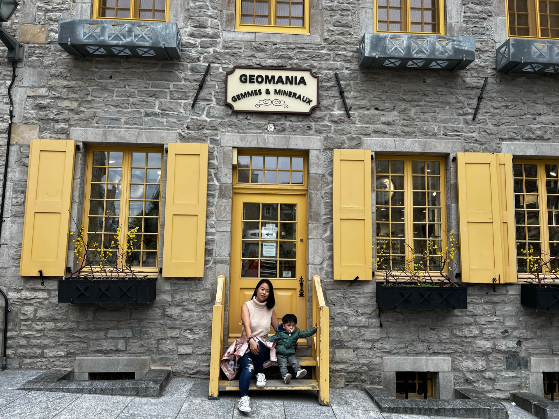 Mother and child on the steps of a stone storefront with yellow shutters