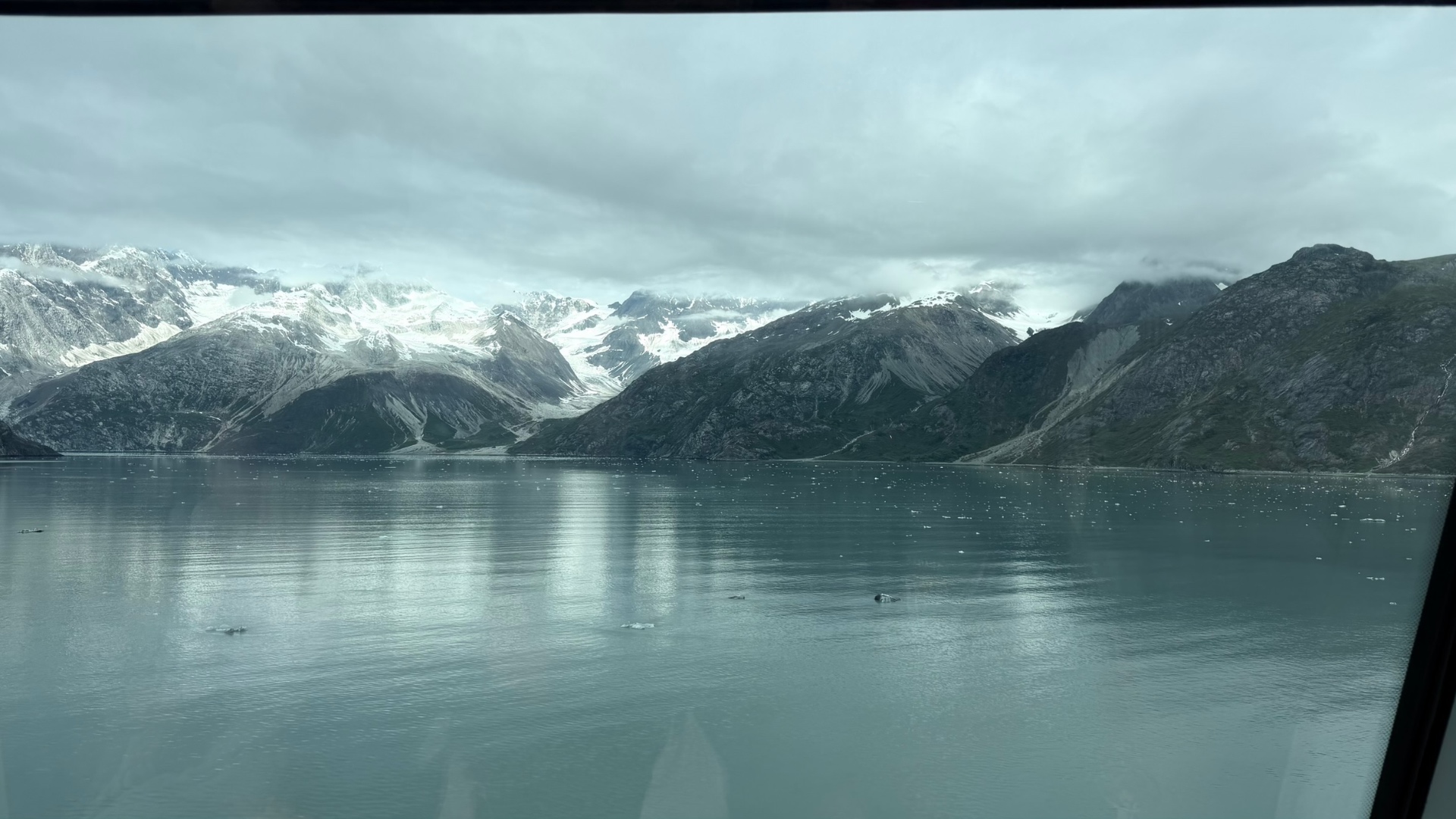 Glacier Bay's calm water and snow-covered mountains beneath a low grey sky
