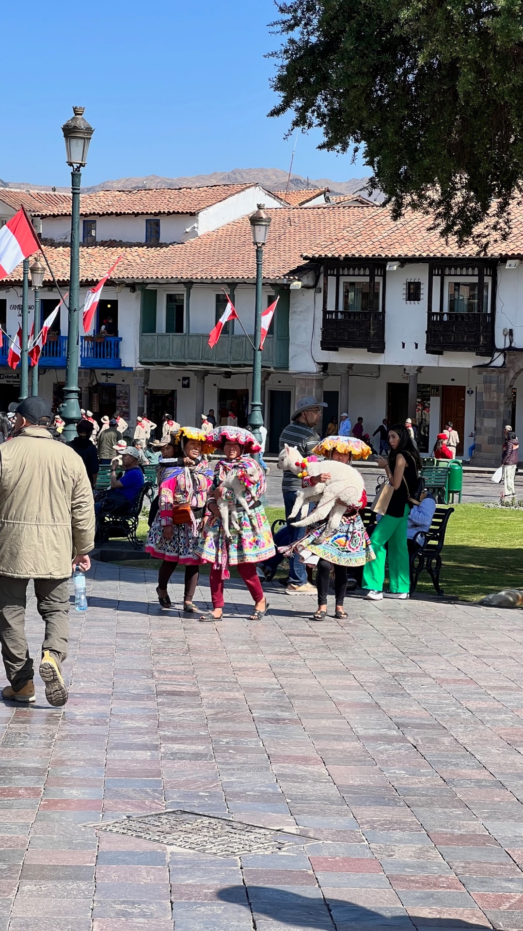 Women in colourful traditional dress carrying alpacas in a colonial square in Cusco