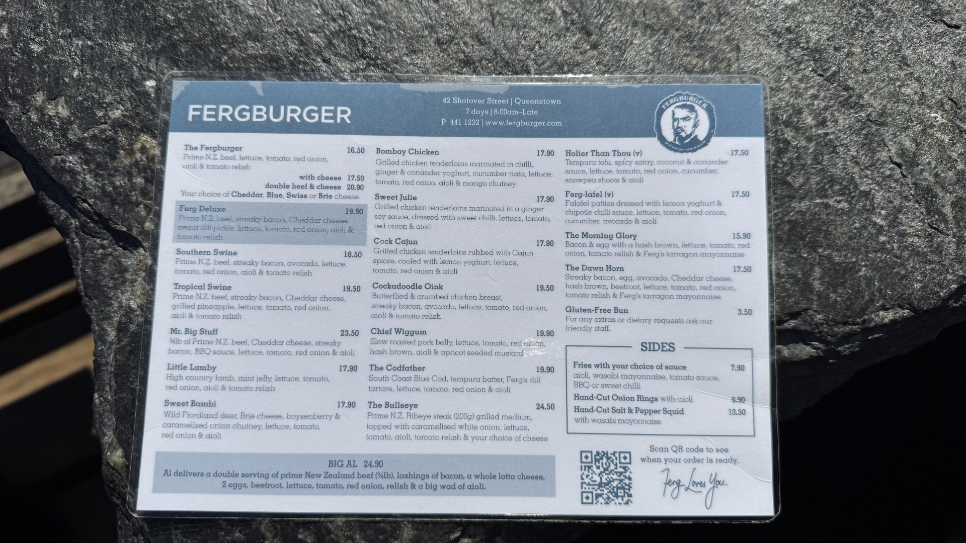 A close-up of the Fergburger menu showing burger choices, prices, the Shotover Street address, and a QR code