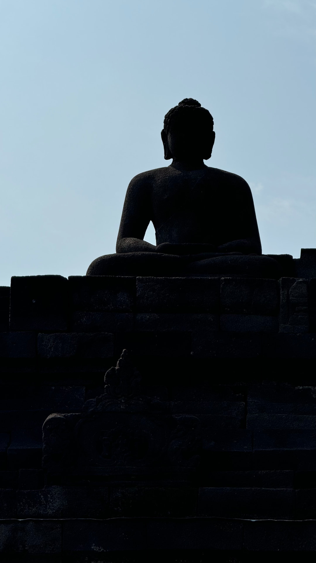 Silhouette of a seated Buddha against the bright sky