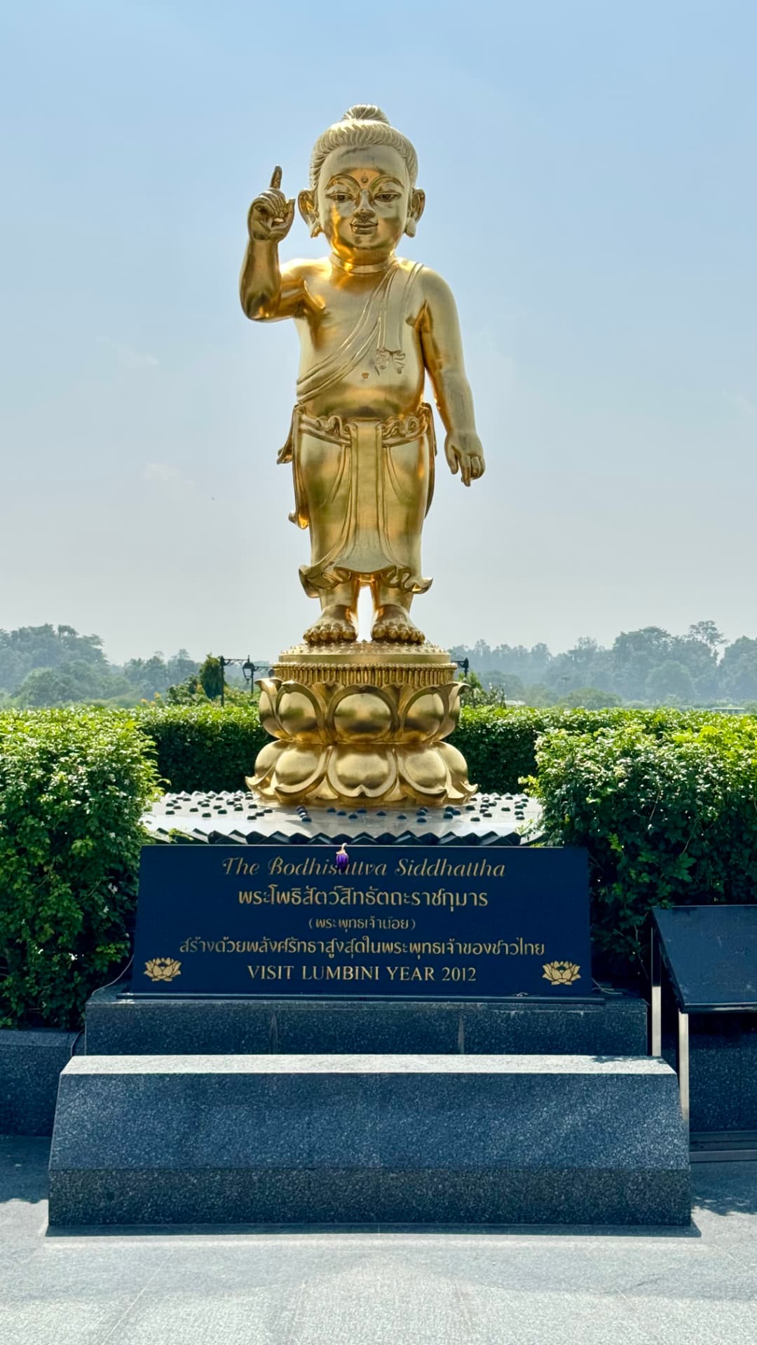 A golden infant Buddha statue stands above a garden pedestal. — Lumbini, Nepal.