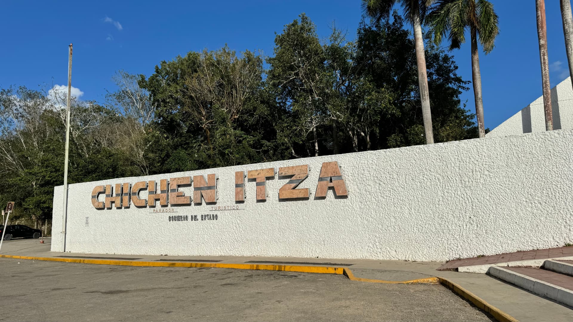Chichén Itzá arrival sign beside palms and forest