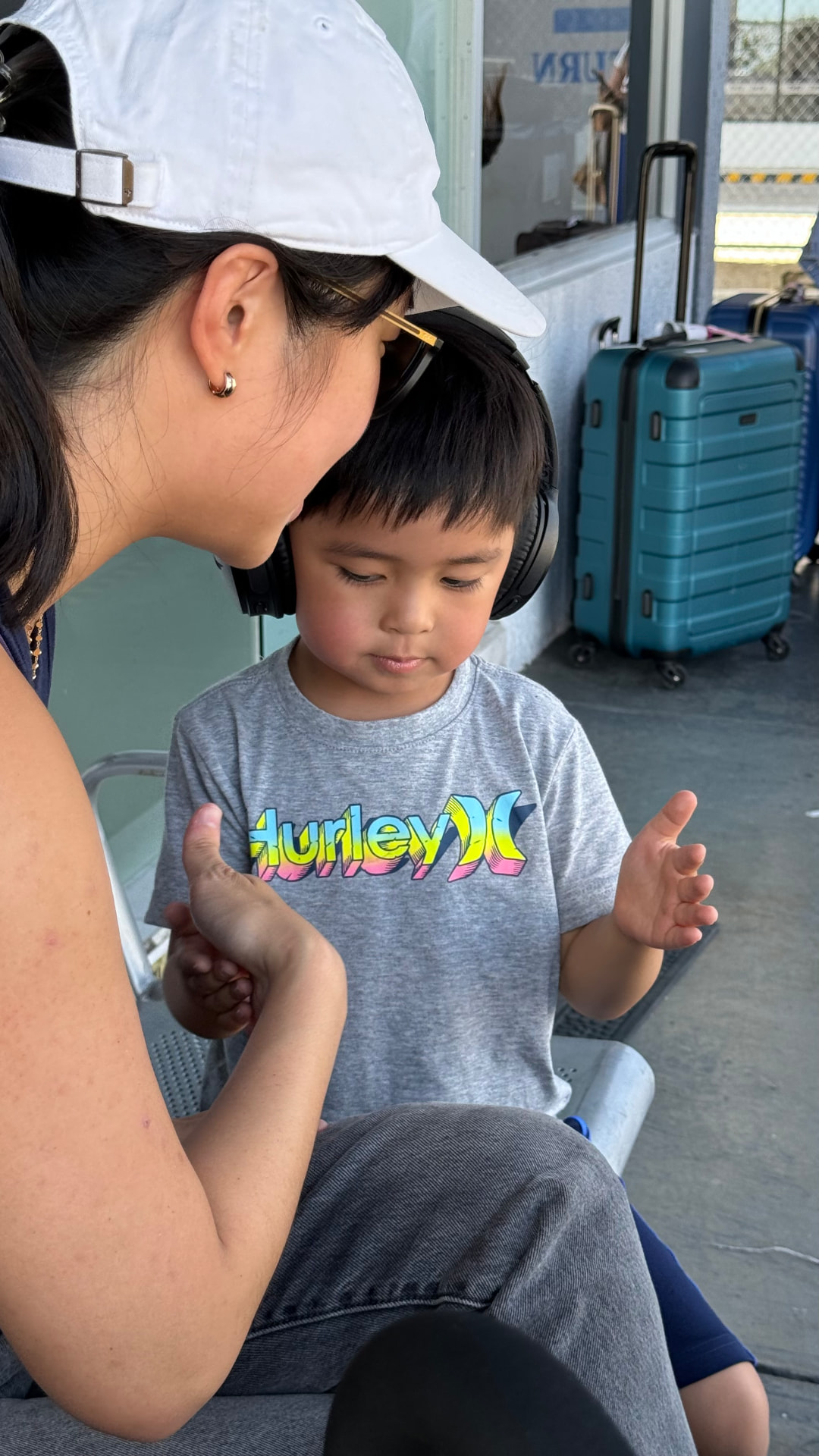 A woman helping a young boy wearing headphones while waiting with luggage