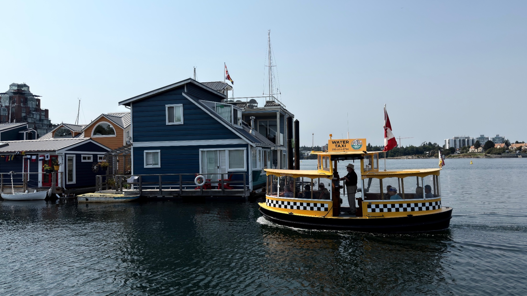 A yellow water taxi passing colourful floating homes in Victoria's harbour
