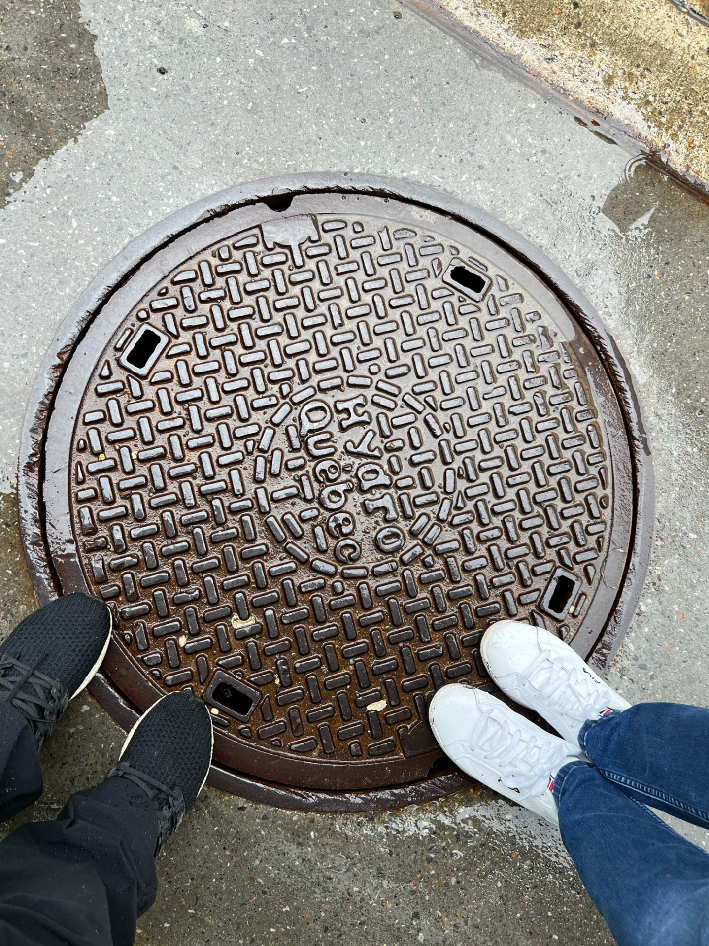 Two pairs of shoes beside a Québec City manhole cover in the pavement