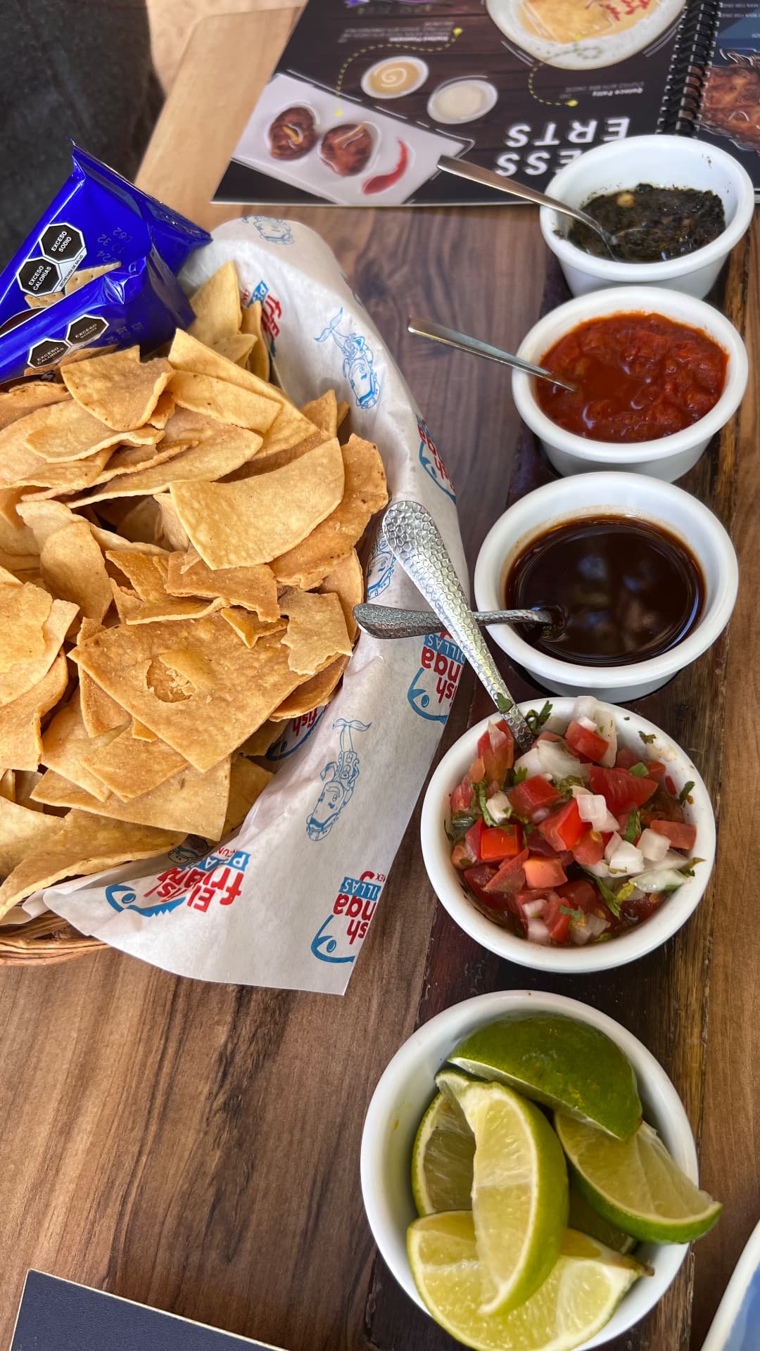 Basket of tortilla chips with five salsas and lime wedges