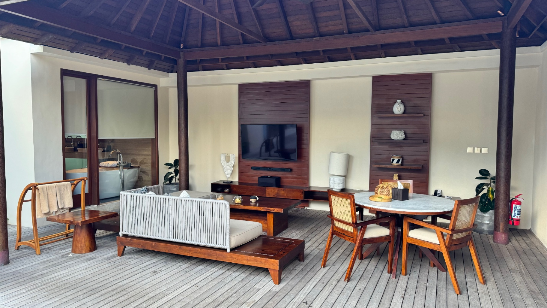 Open-sided villa pavilion with timber roof beams, sofa, dining table and deck