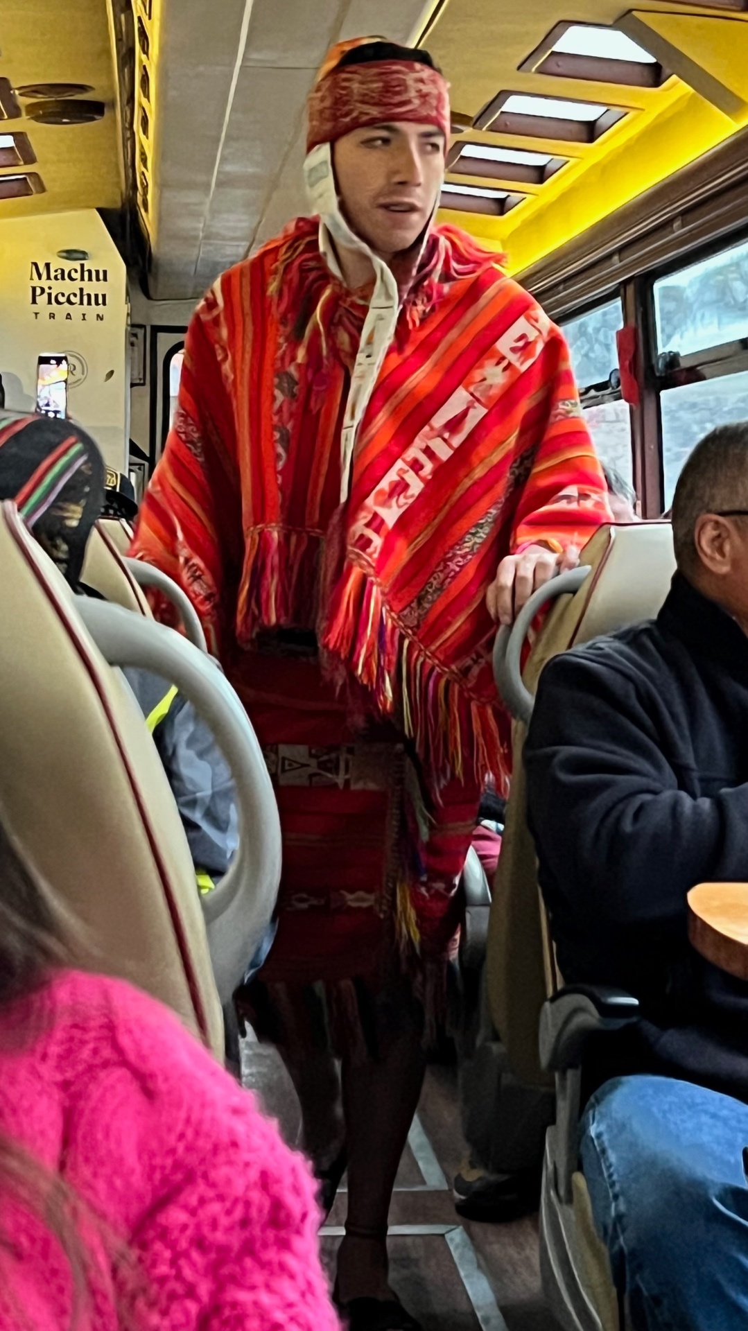 Male performer in vivid red Andean clothing entertaining passengers aboard the Machu Picchu train