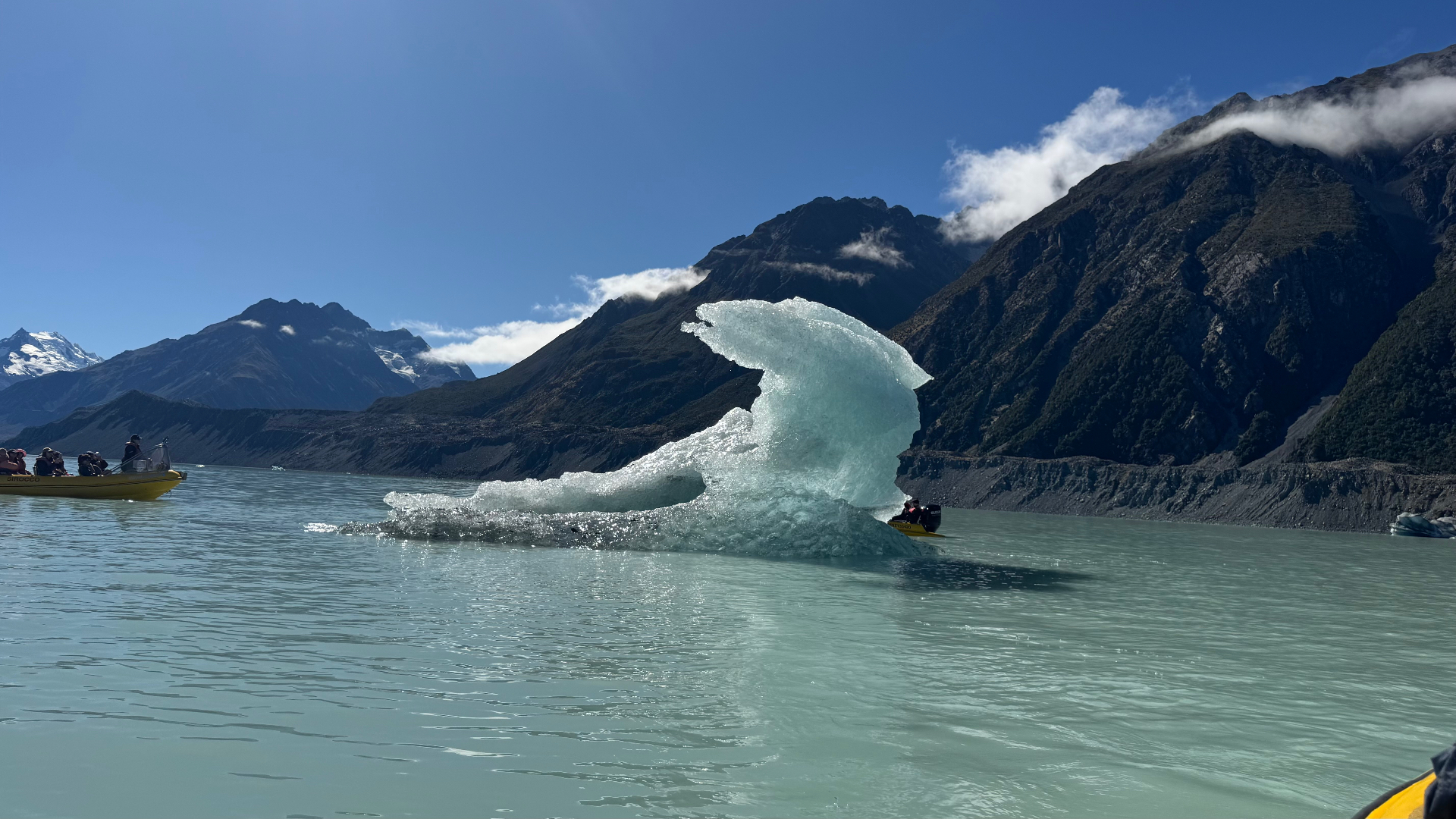 A large curved iceberg floating in the pale green glacial lake with a second tour boat behind it